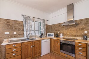 A compact kitchen with a brick backsplash, wooden cabinets, a stainless steel range hood, a microwave, and a dishwasher.