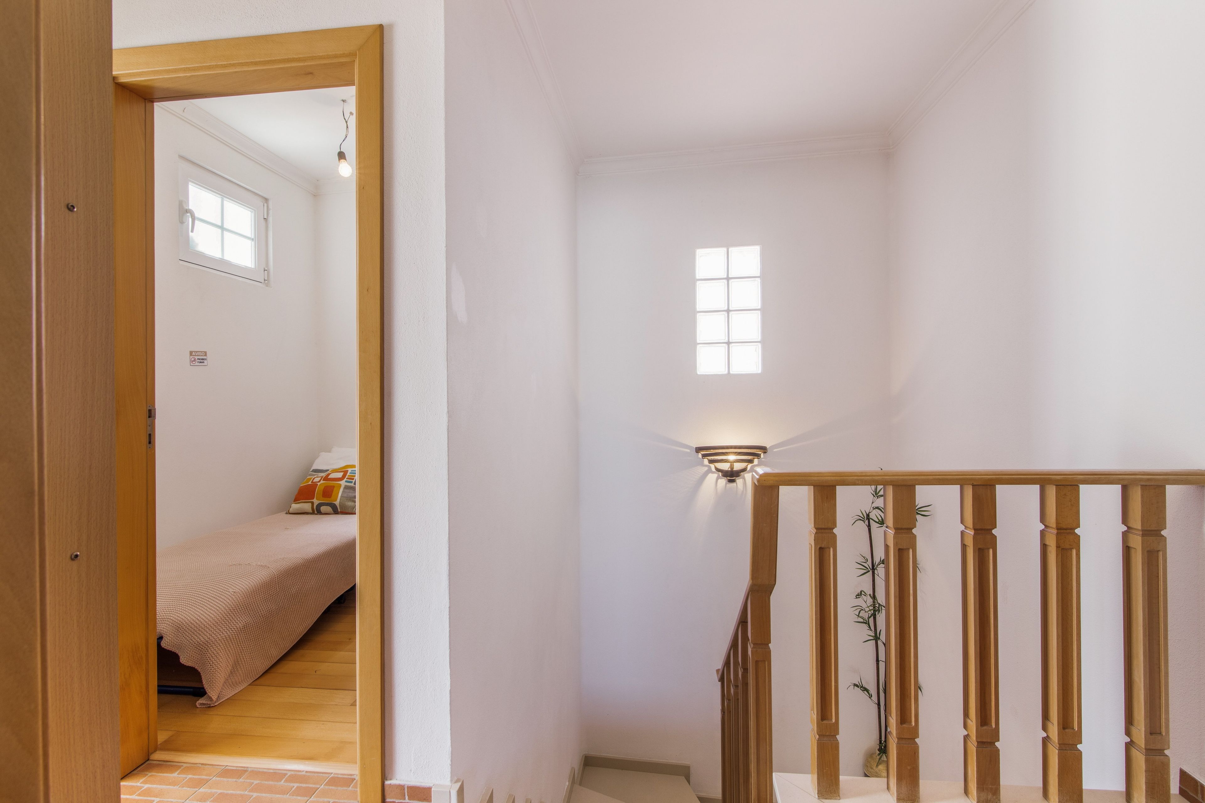 Un pasillo estrecho con un marco de puerta de madera, un ventanal pequeño y un aplique en la pared.