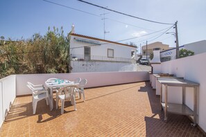 A rooftop terrace with a table and chairs, a small sink, and a view of a building with a tiled roof.
