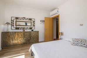 A bedroom with a bed, a wooden cabinet, a mirror, and an air conditioning unit.