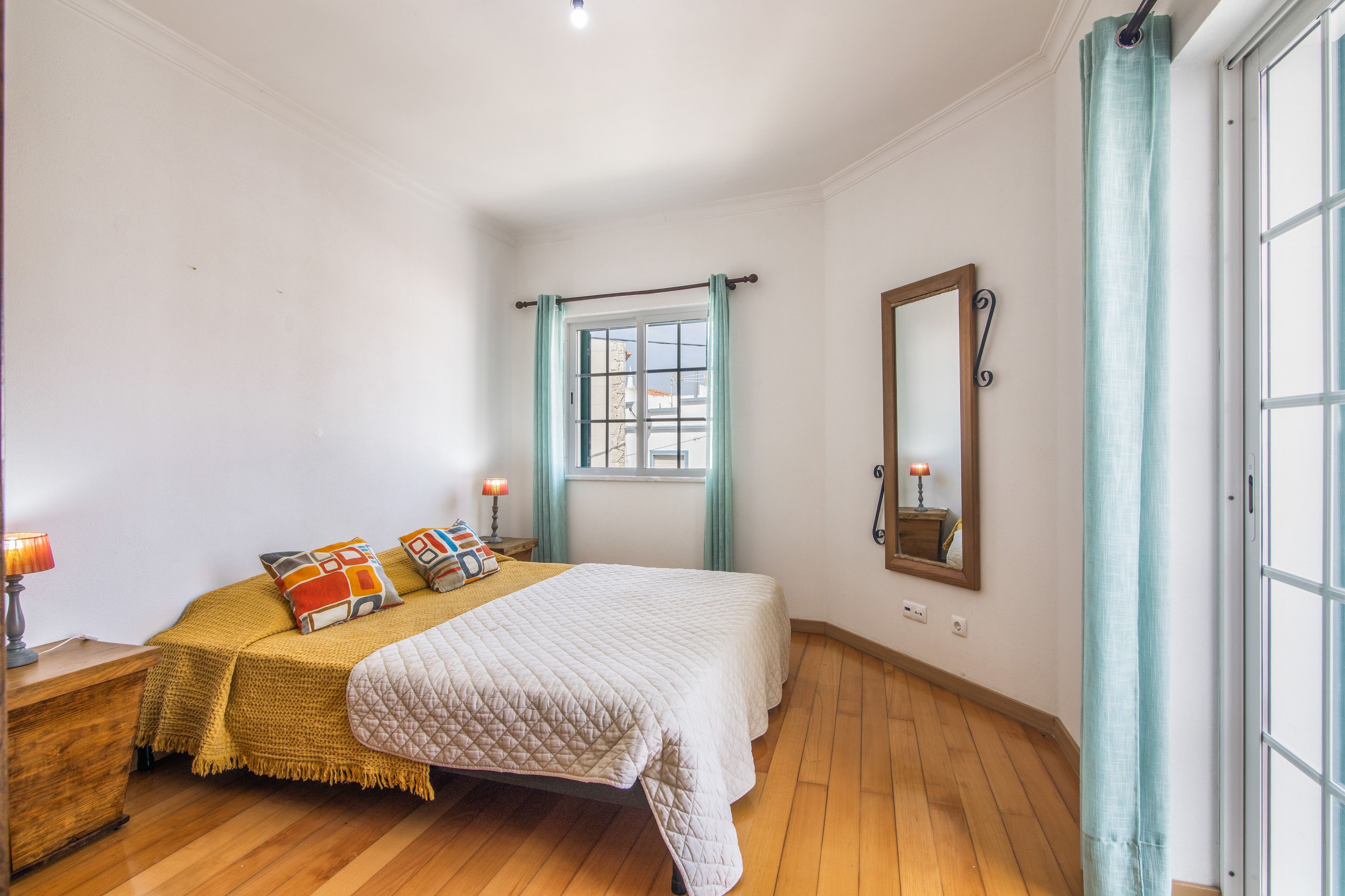 A bedroom with a bed, bedside lamps, a mirror, and a window with curtains.