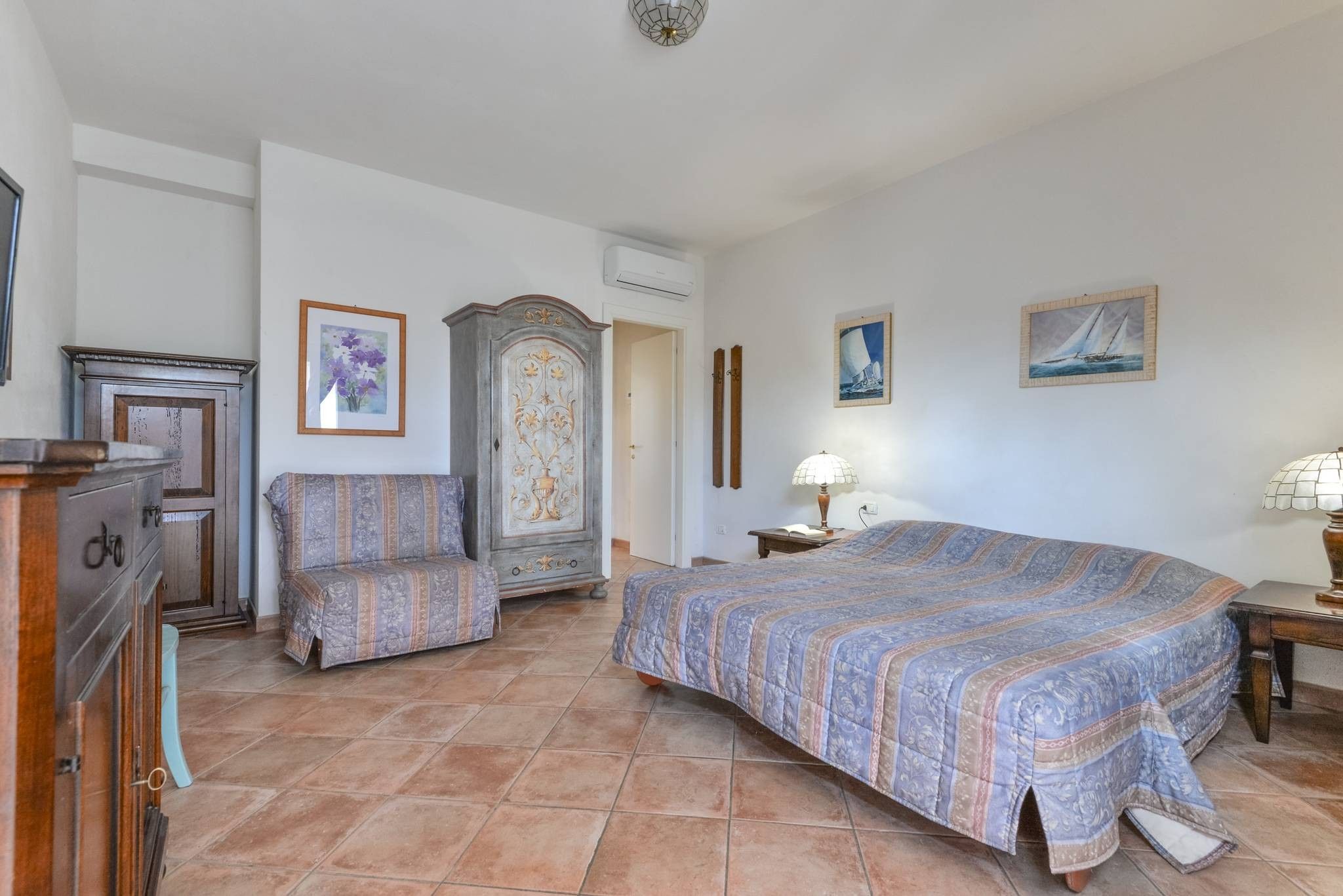 Un dormitorio con una cama grande, una silla, un aparador y un armario.