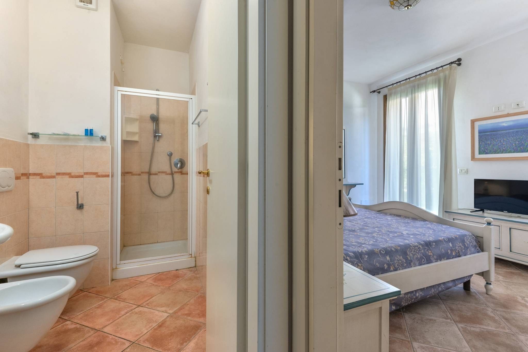 A hotel room with a shower, toilet, bed, and a television.