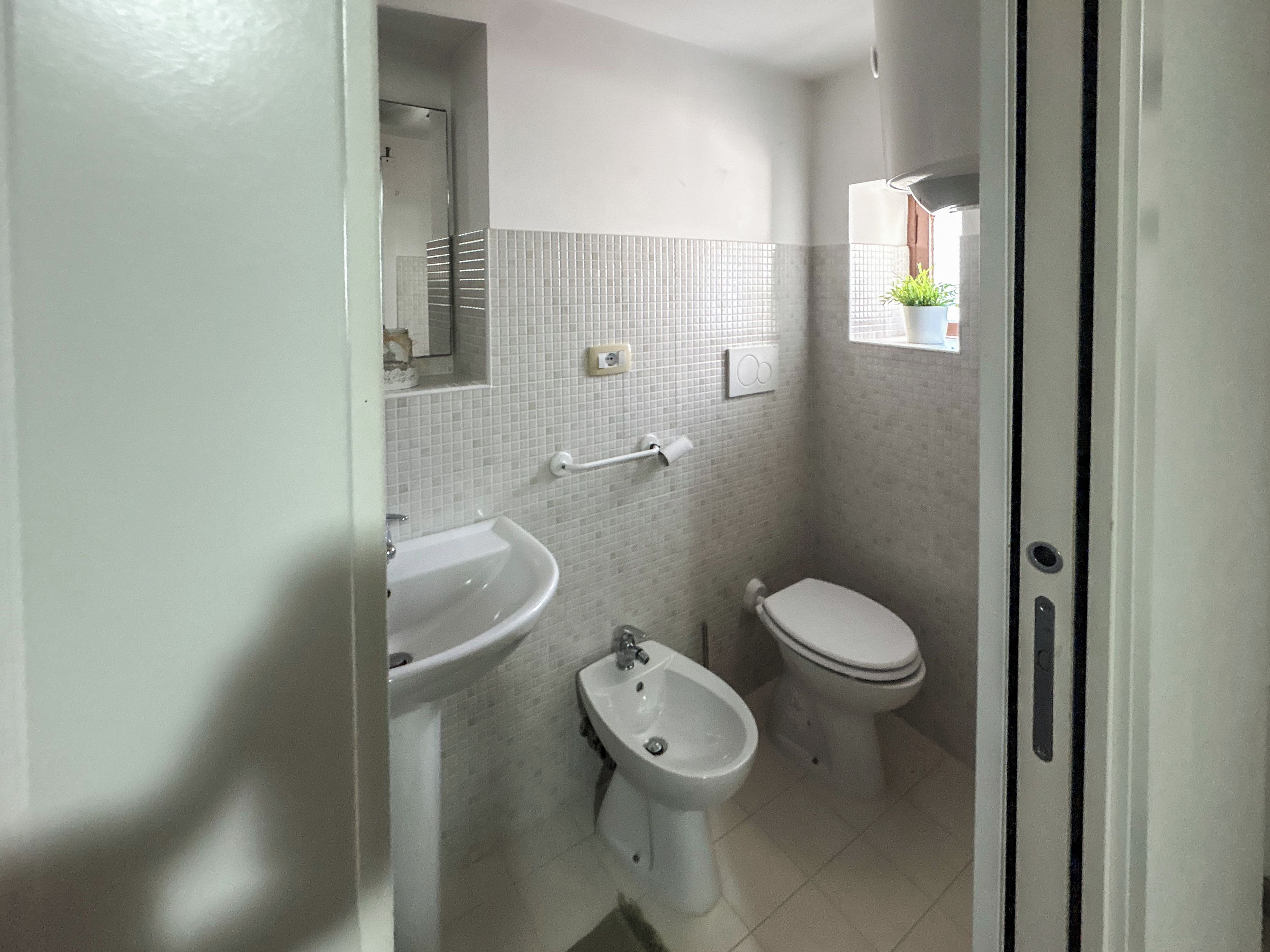 A bathroom with a sink, bidet, toilet, and a window with a plant.