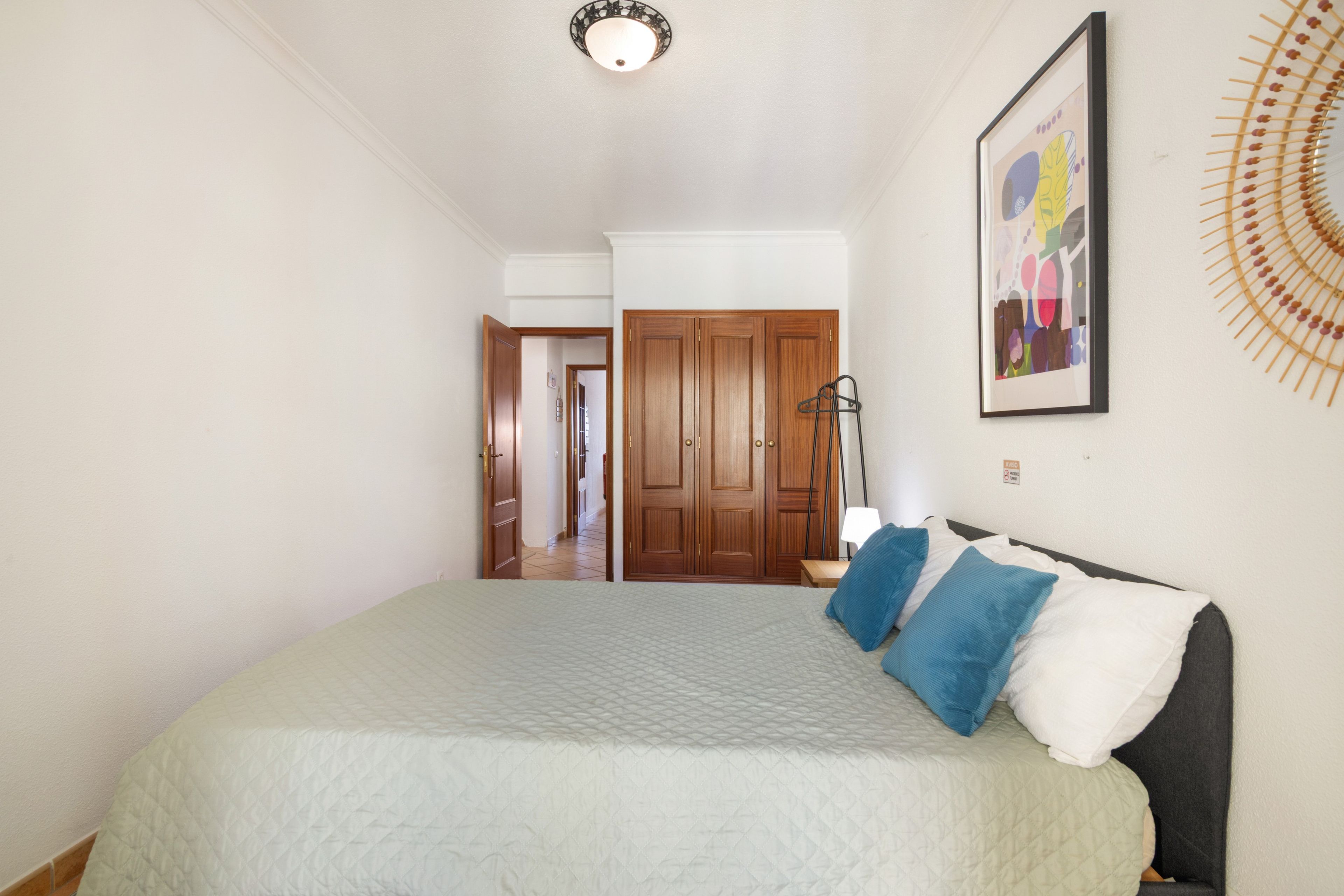 A bedroom with a bed, a wardrobe, and a door leading to another room.