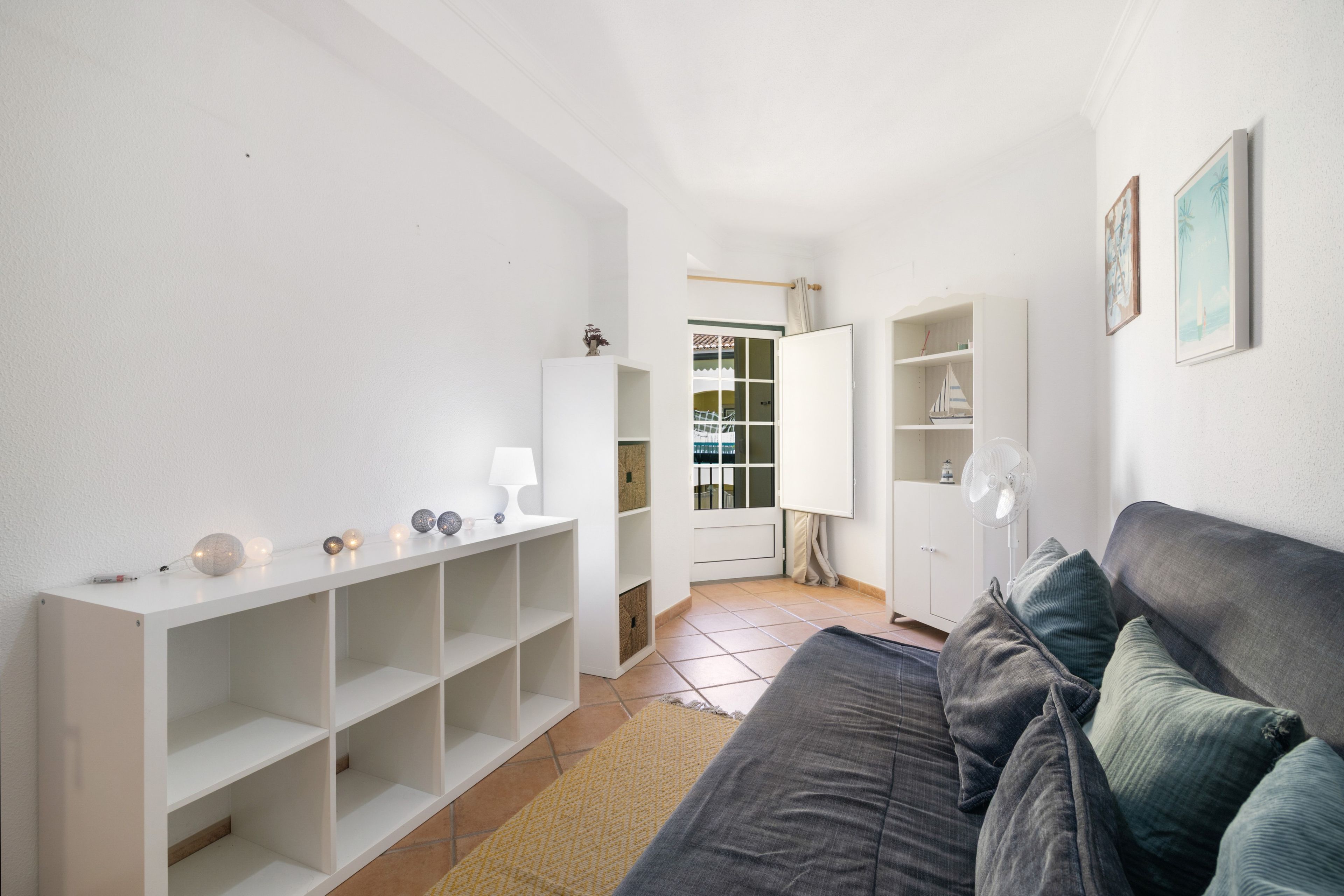 Un salon moderne avec un canapé gris, une étagère blanche et une petite table agrémentée d’objets décoratifs.