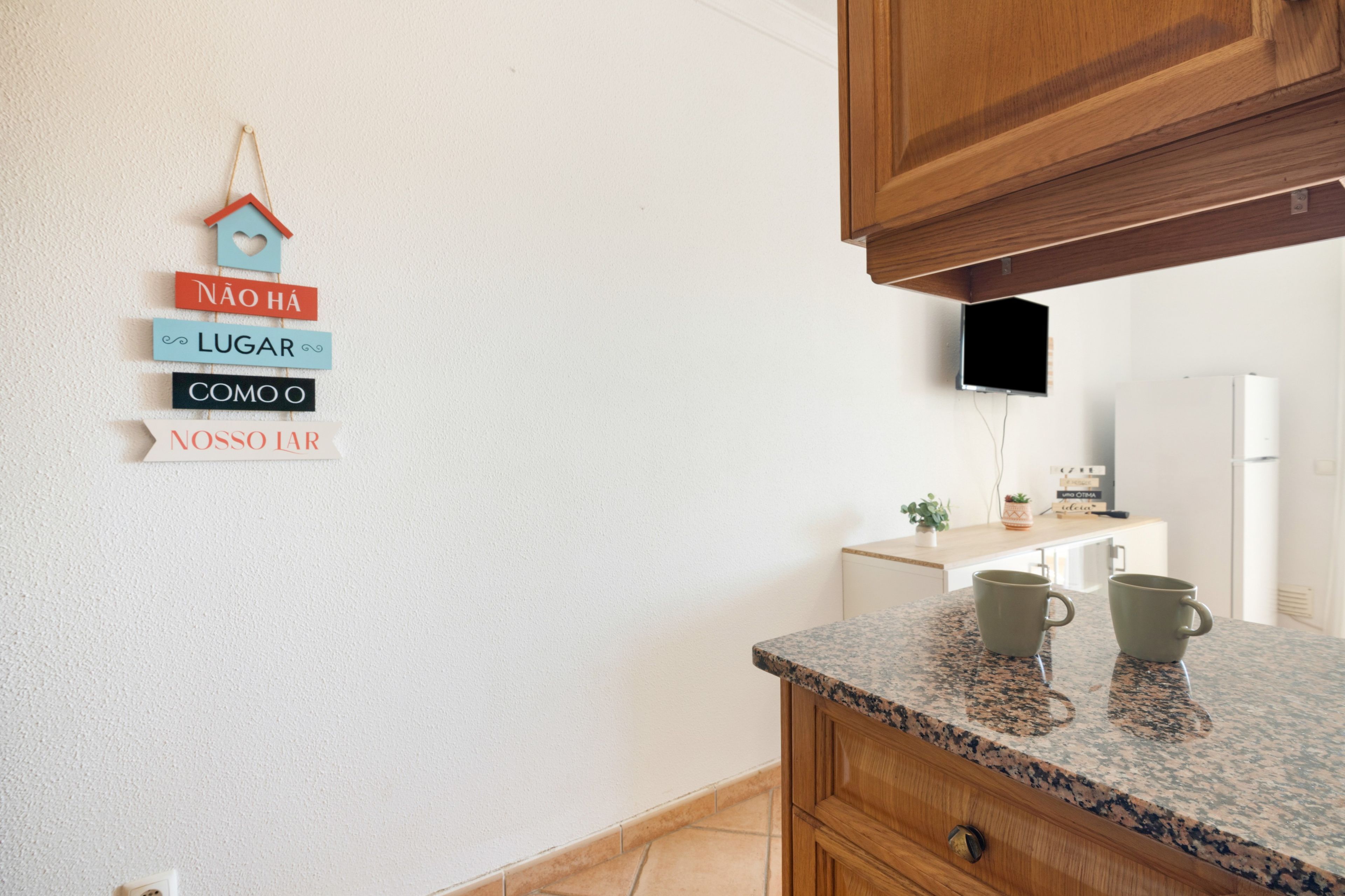 Een keuken met houten kastjes, een granieten aanrechtblad en een aan de muur bevestigde televisie.