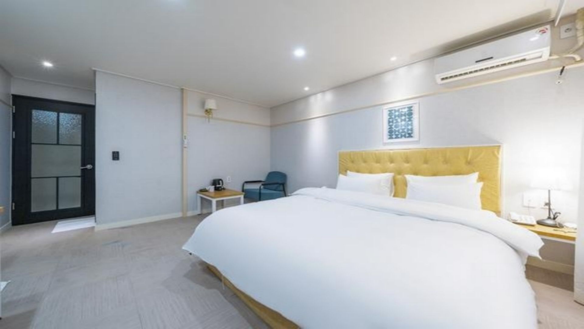 A hotel room with a large bed, a desk, a chair, and a door.