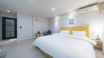 A hotel room with a large bed, a desk, a chair, and a door.