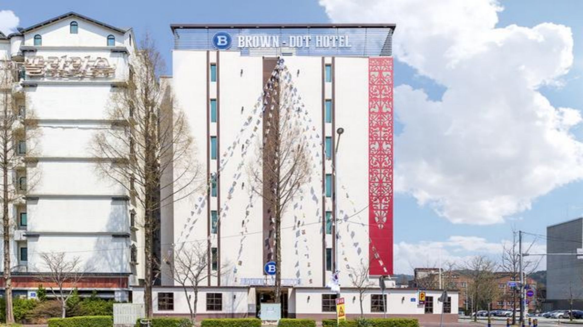 A hotel building with a prominent 'BROWN-DOT HOTEL' sign, a parking sign, and a red vertical banner.