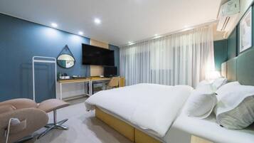 A hotel room with a bed, a desk, a chair, a TV, and a window with curtains.