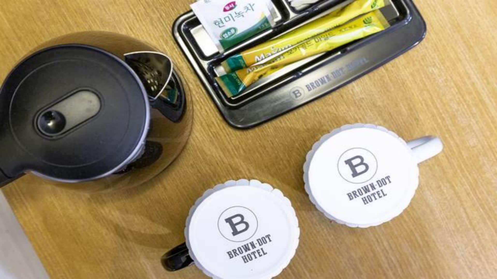Un juego de té con tetera y dos tazas, una bandeja con bolsitas de té y una etiqueta con el texto 'BROWN-DOT HOTEL'.