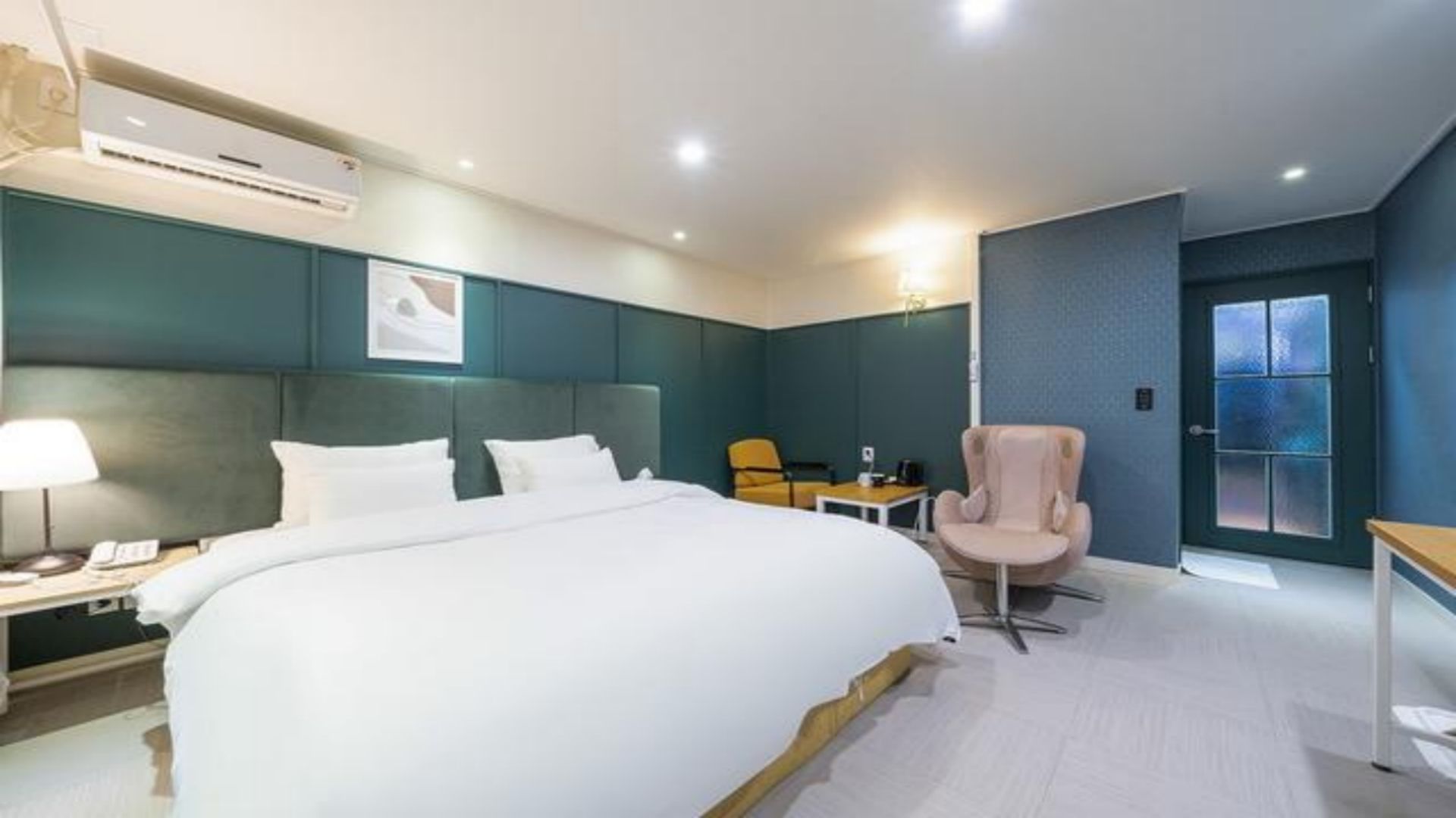 A hotel room with a large bed, a desk, a chair, and a door with frosted glass panels.