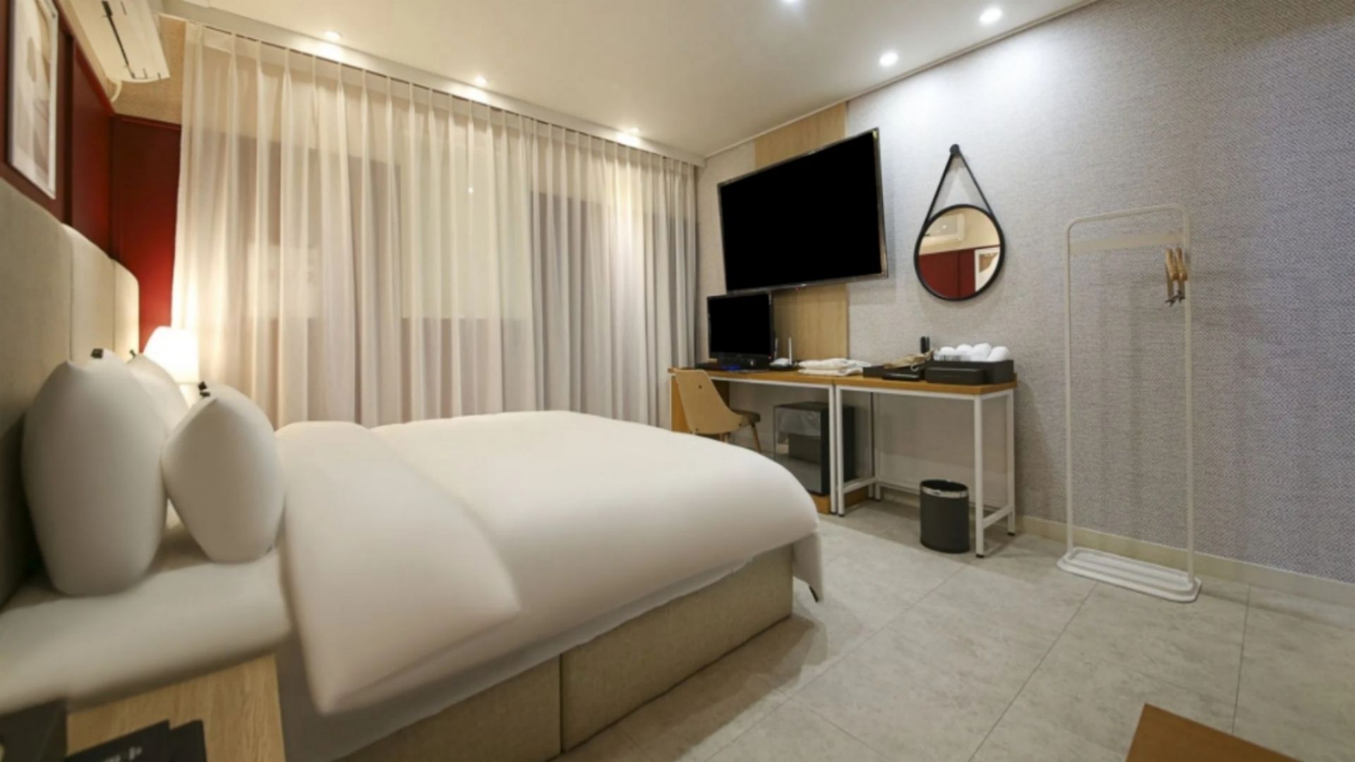Une chambre d’hôtel moderne équipée d’un lit, d’un bureau, d’une télévision et d’un miroir.