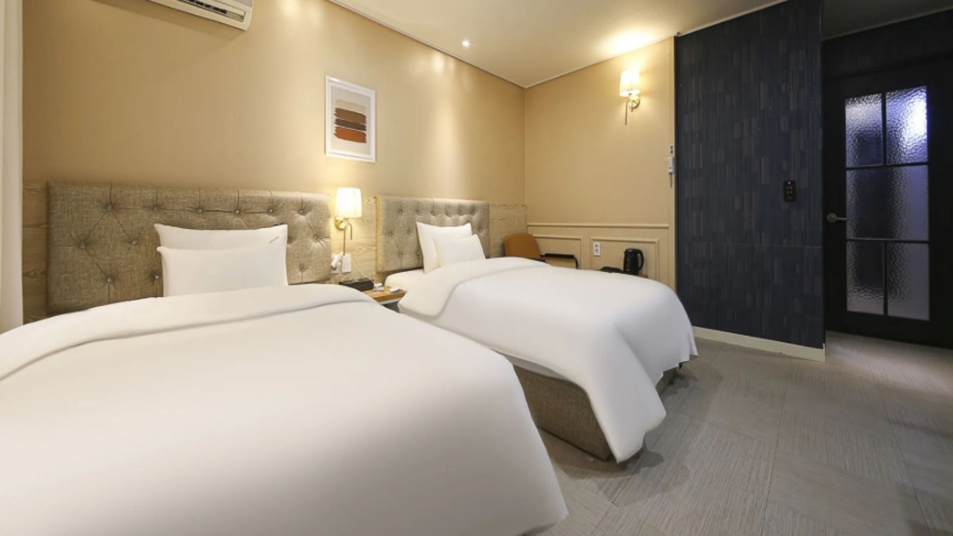 Ein Hotelzimmer mit zwei Betten, einem Nachttisch, einer Wandlampe und einer Tür mit Milchglasfenster.