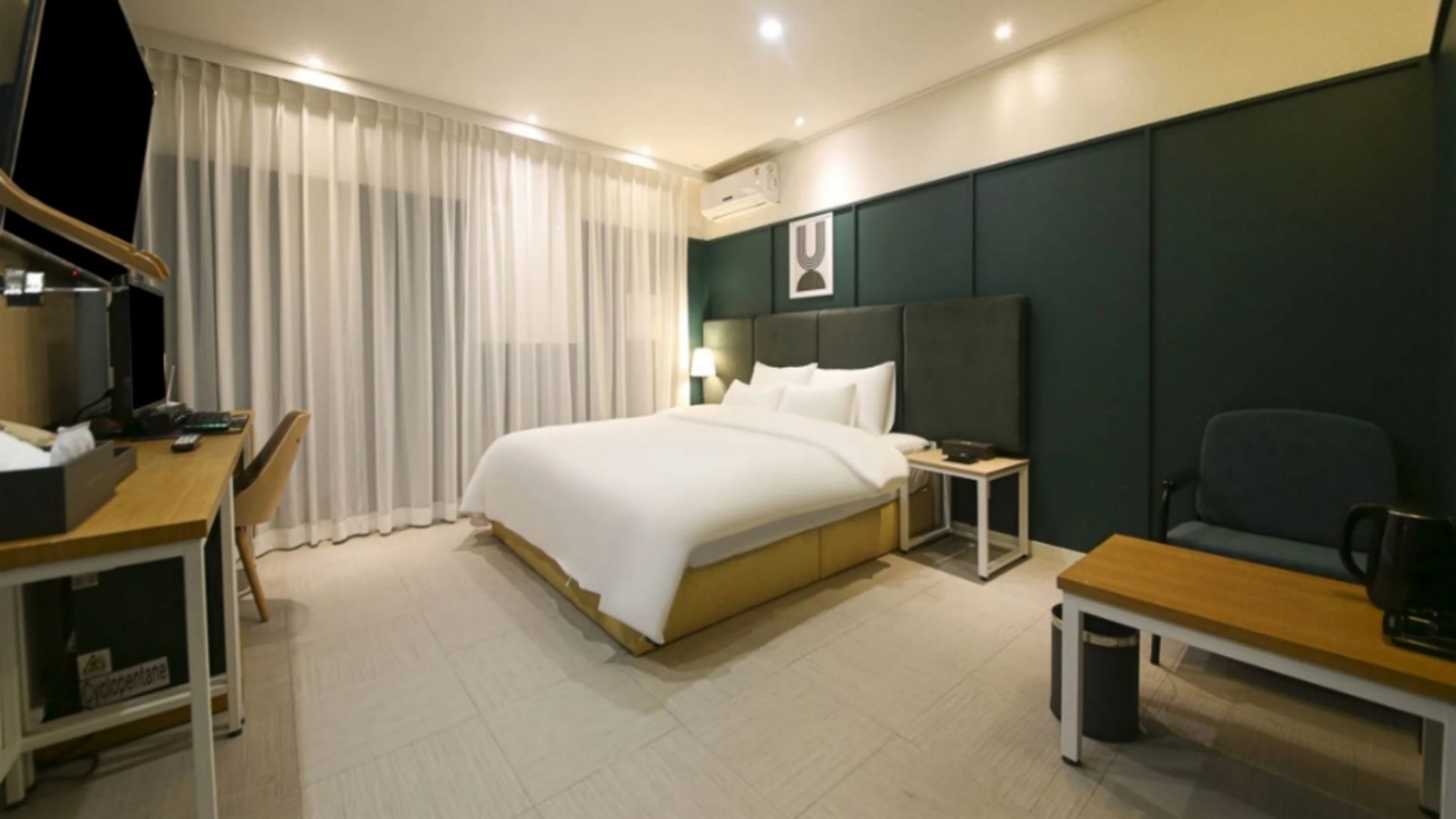 Een hotelkamer met een bed, een bureau, een stoel, een televisie en een raam met gordijnen.