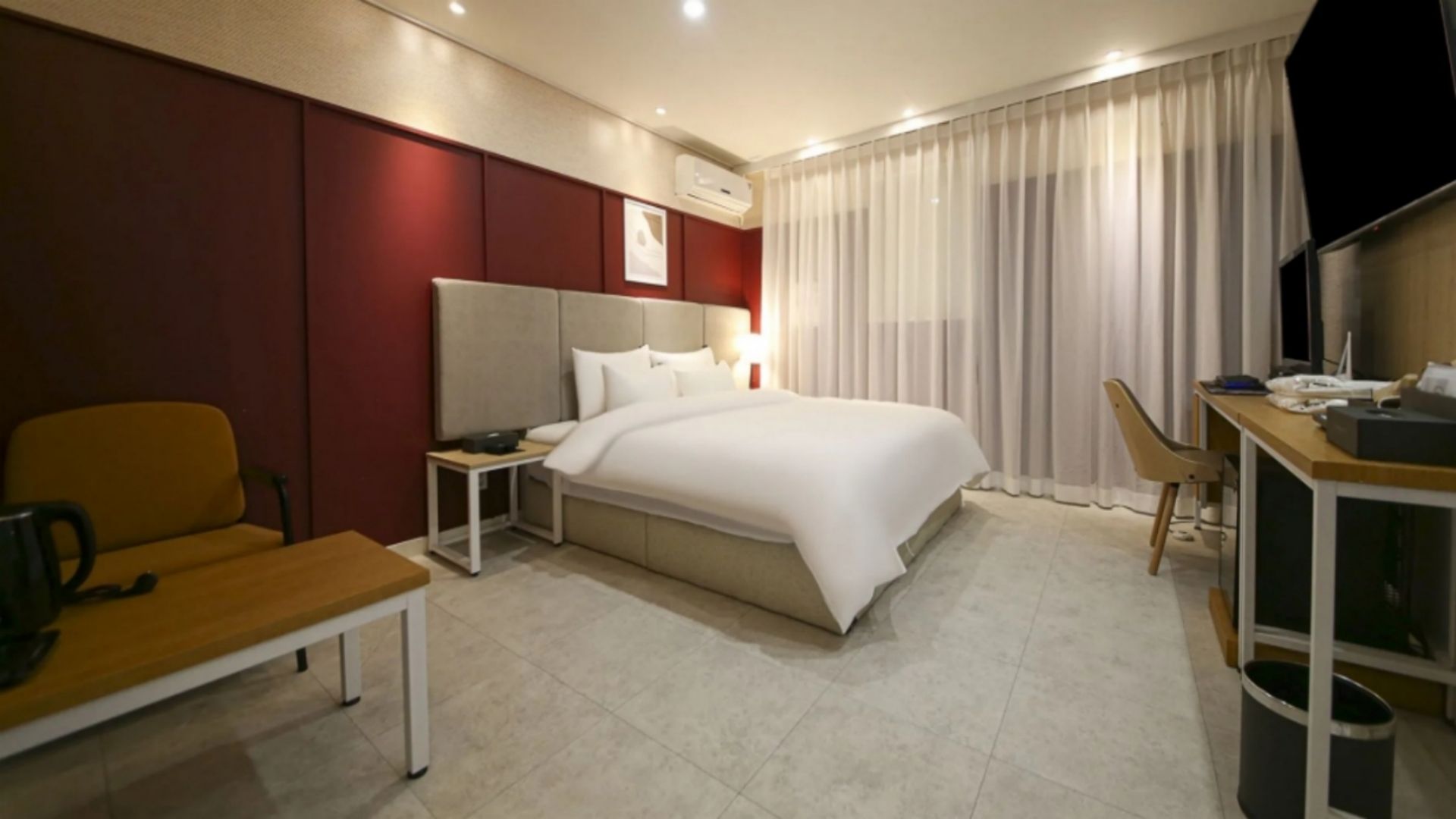A hotel room with a bed, a desk, a chair, a coffee table, and a TV.