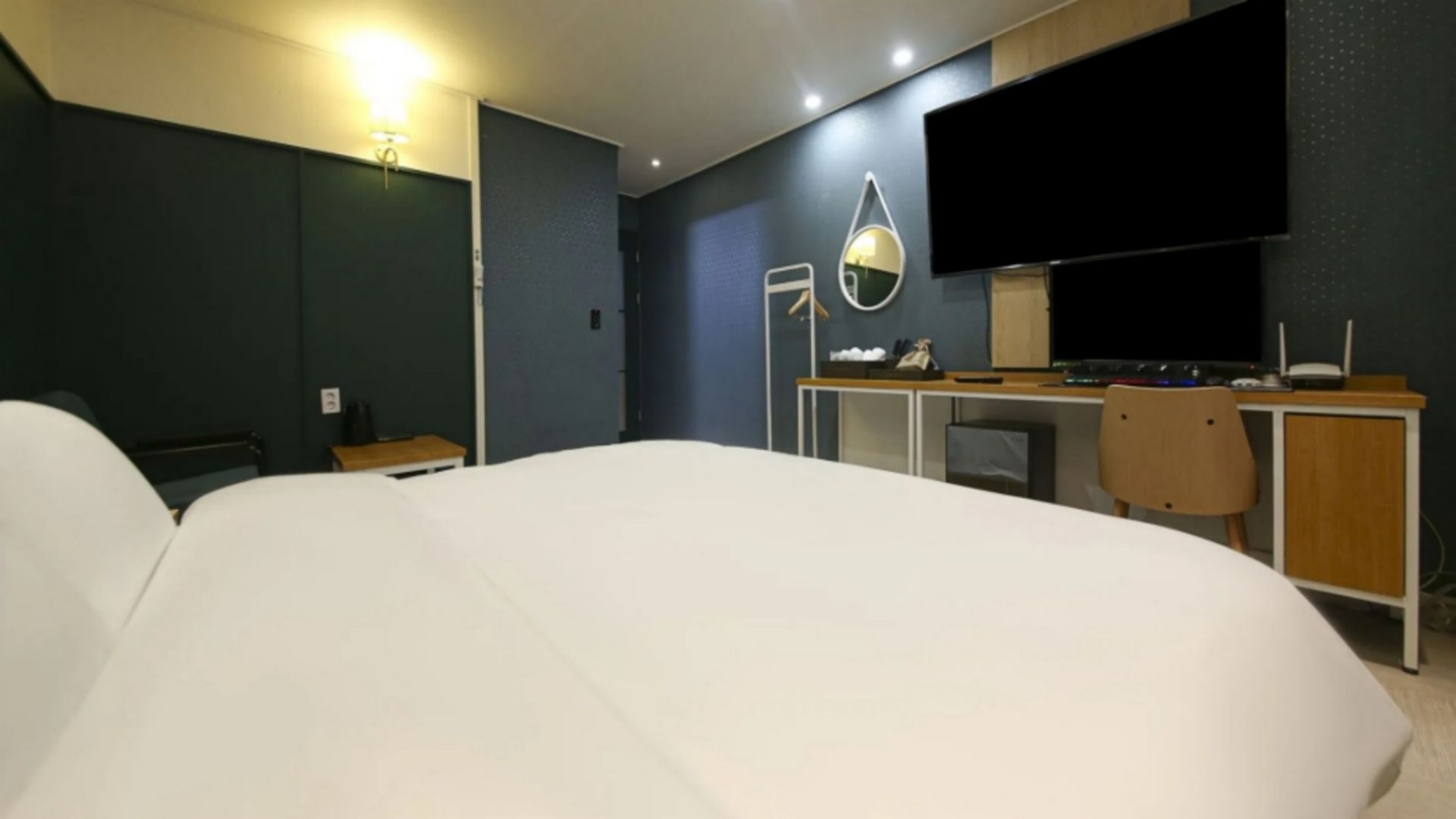 Habitación de hotel con una cama grande, un escritorio con computadora, una silla, un televisor de pantalla plana y un espejo.