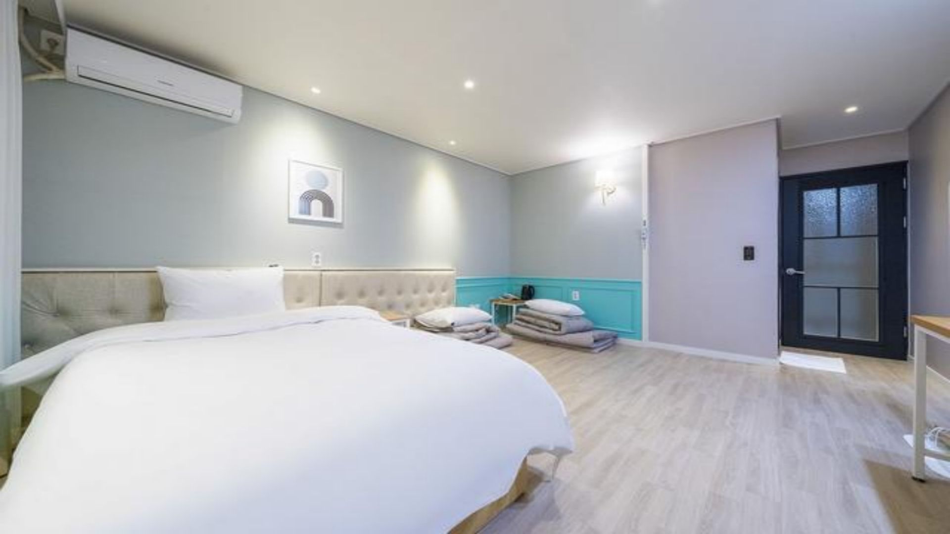 A hotel room with a large bed, a bedside table, a chair, and a door with frosted glass panels.