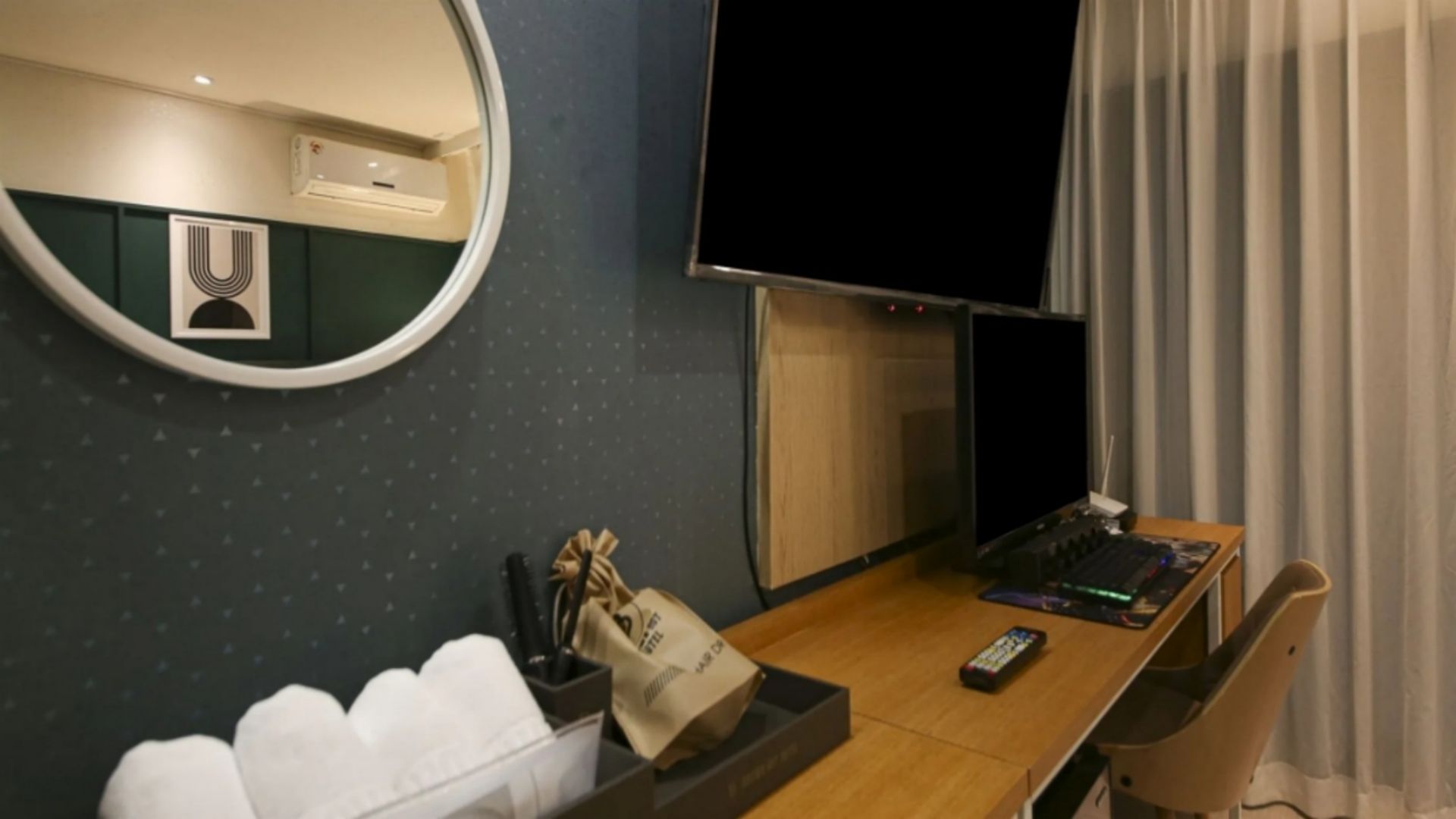 A hotel room with a bed, a desk with a computer, a TV, and a mirror.