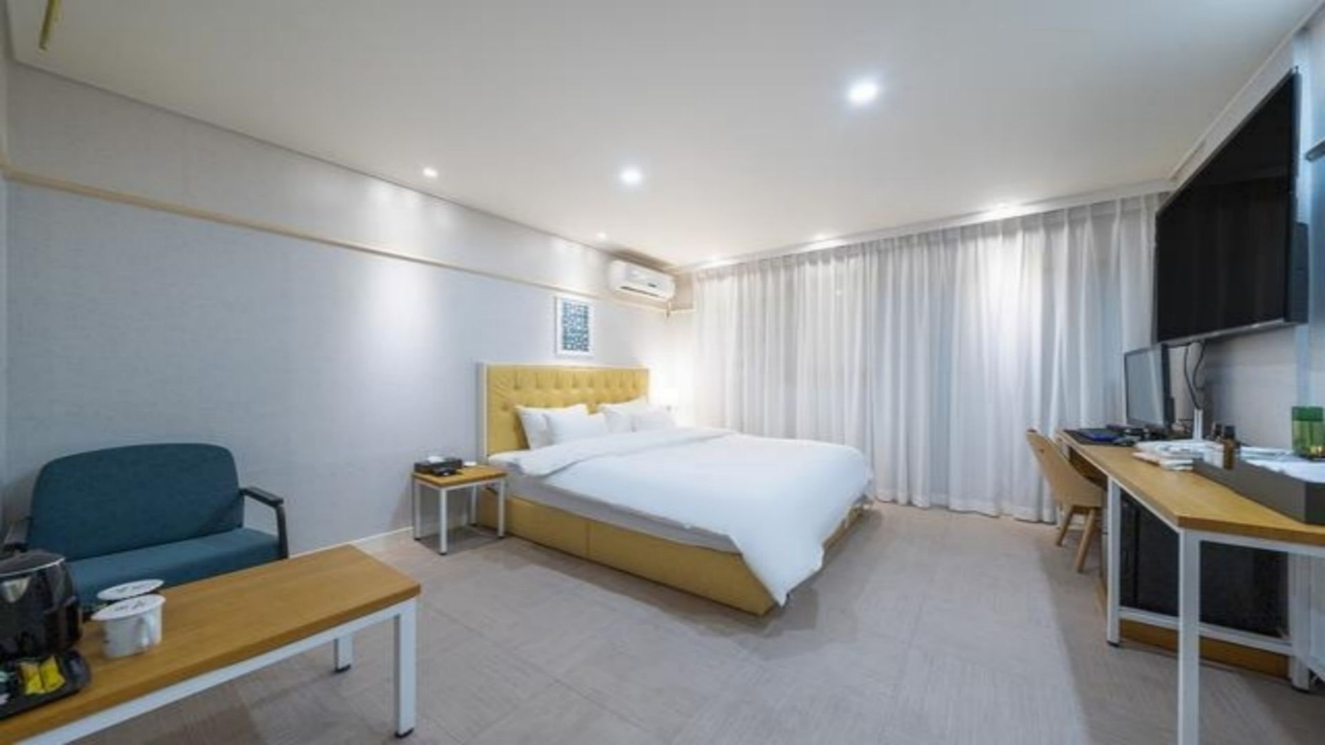 Quarto de hotel com cama, escrivaninha, cadeira e televisão.