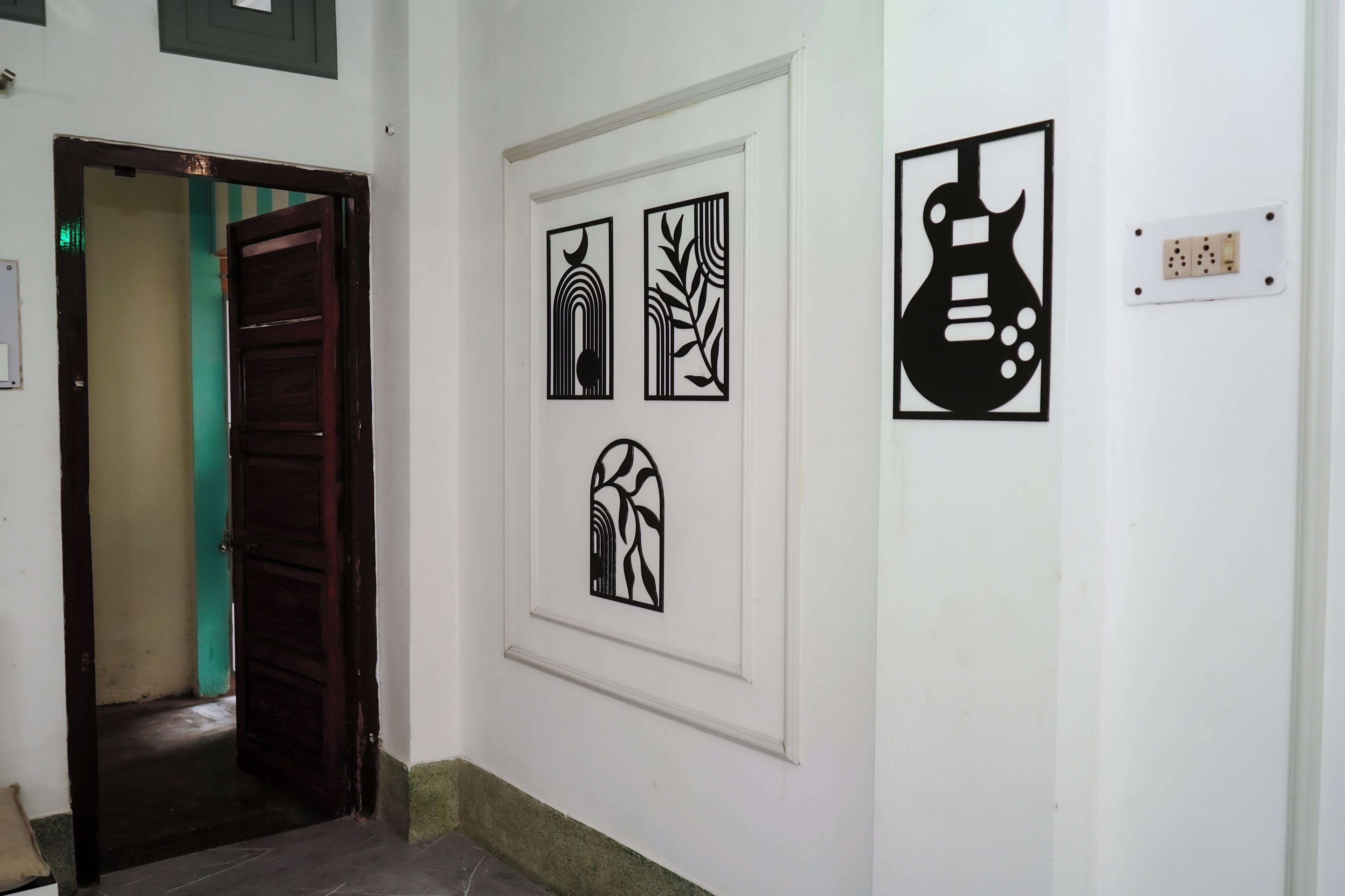 A hallway with a wooden door, a white wall with four black framed artworks, and a light switch.