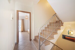 Un escalier avec des rampes en métal menant à l’étage supérieur, une porte donnant sur une autre pièce et un luminaire suspendu.