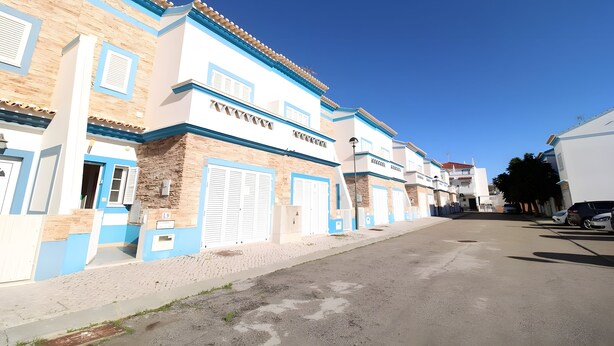 Uma fileira de edifícios com fachadas azuis e brancas, grandes portões de garagem e um céu claro.