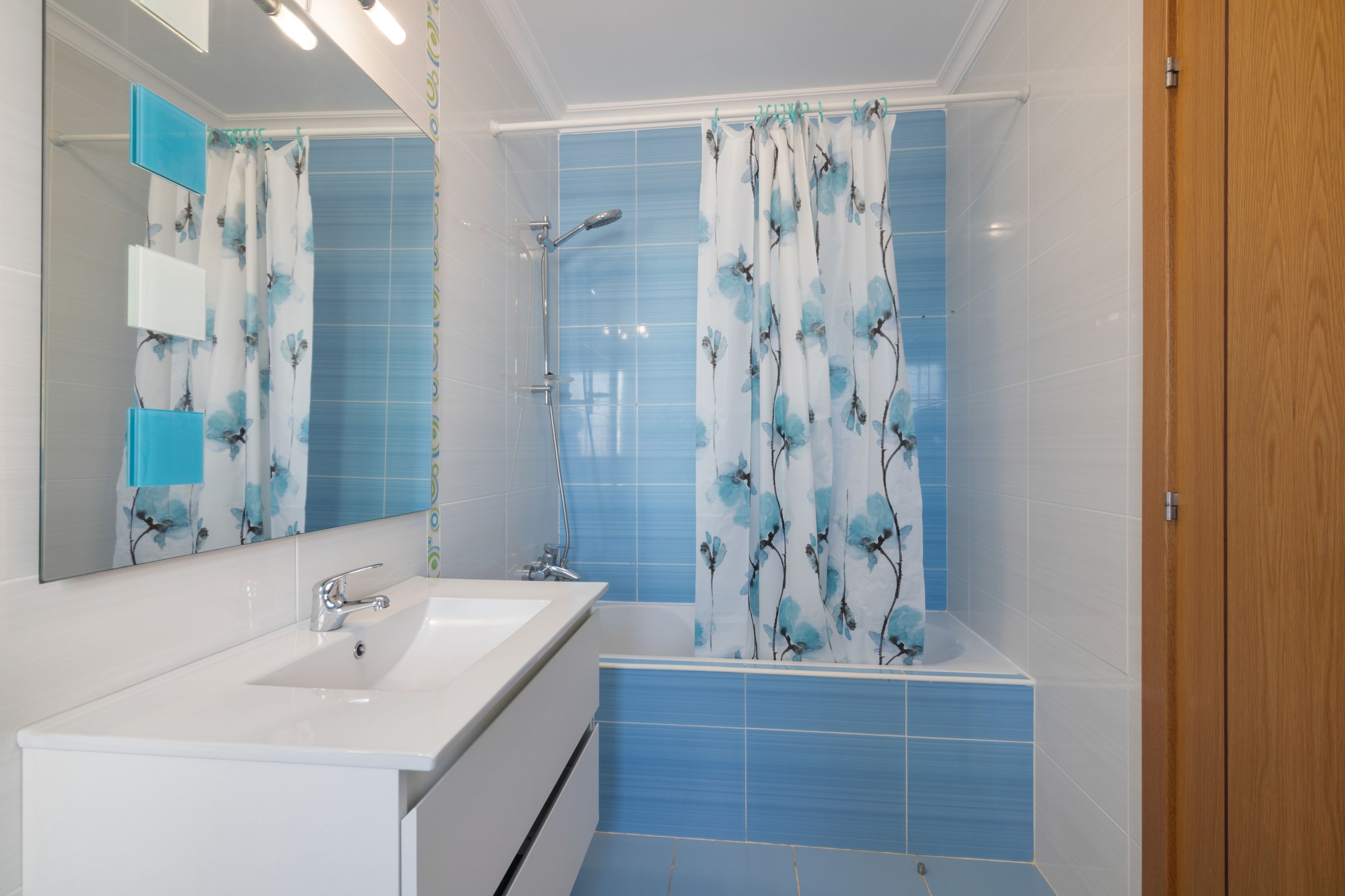 Un baño con un lavabo blanco, un espejo, una ducha con cortina azul y una puerta de madera.