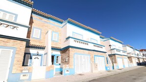 Fileira de edifícios com fachadas azuis e brancas, várias portas de garagem e céu claro.