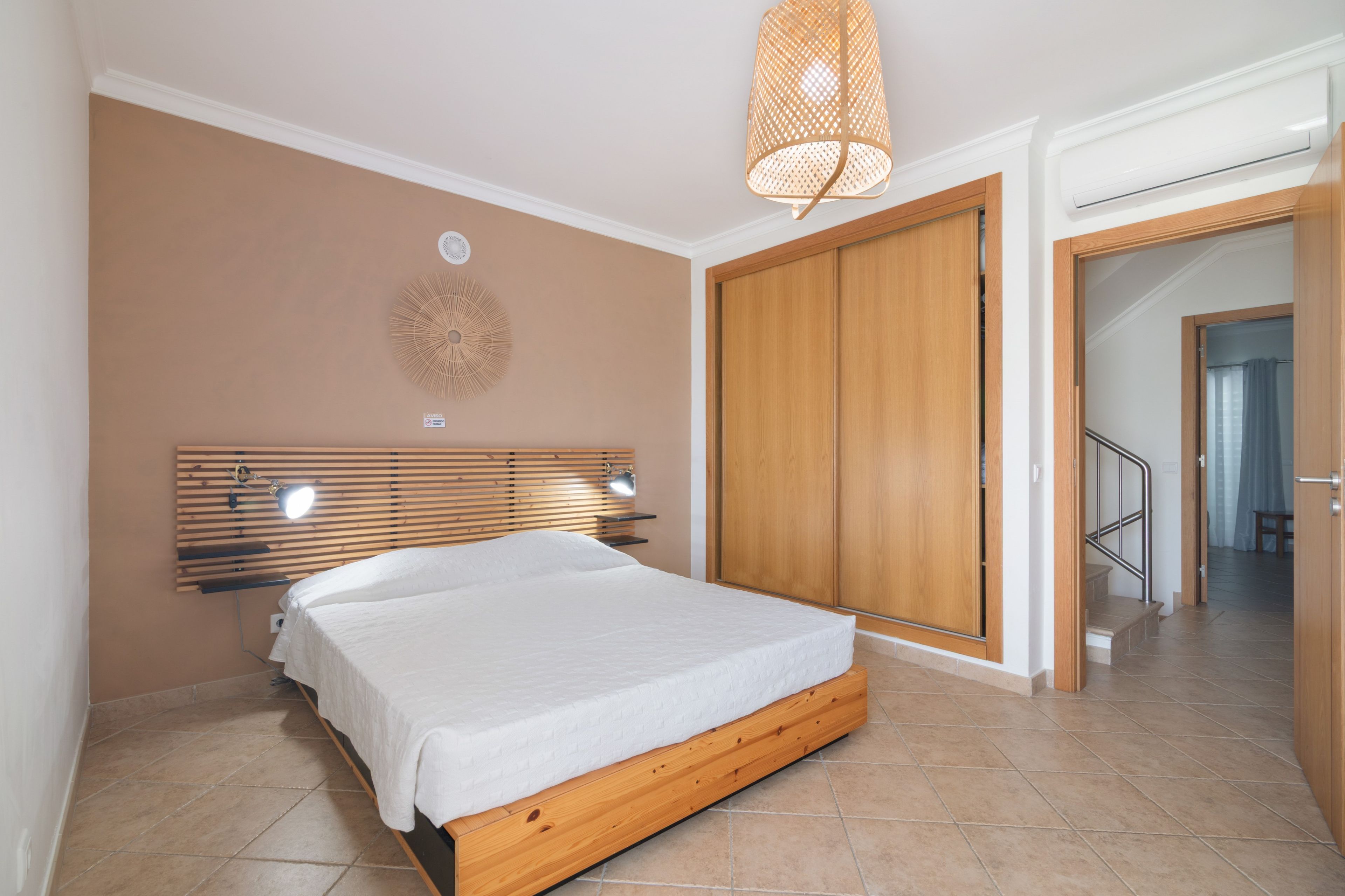 Un dormitorio con cama de madera, ventilador de techo, armario y una escalera que lleva a otra habitación.