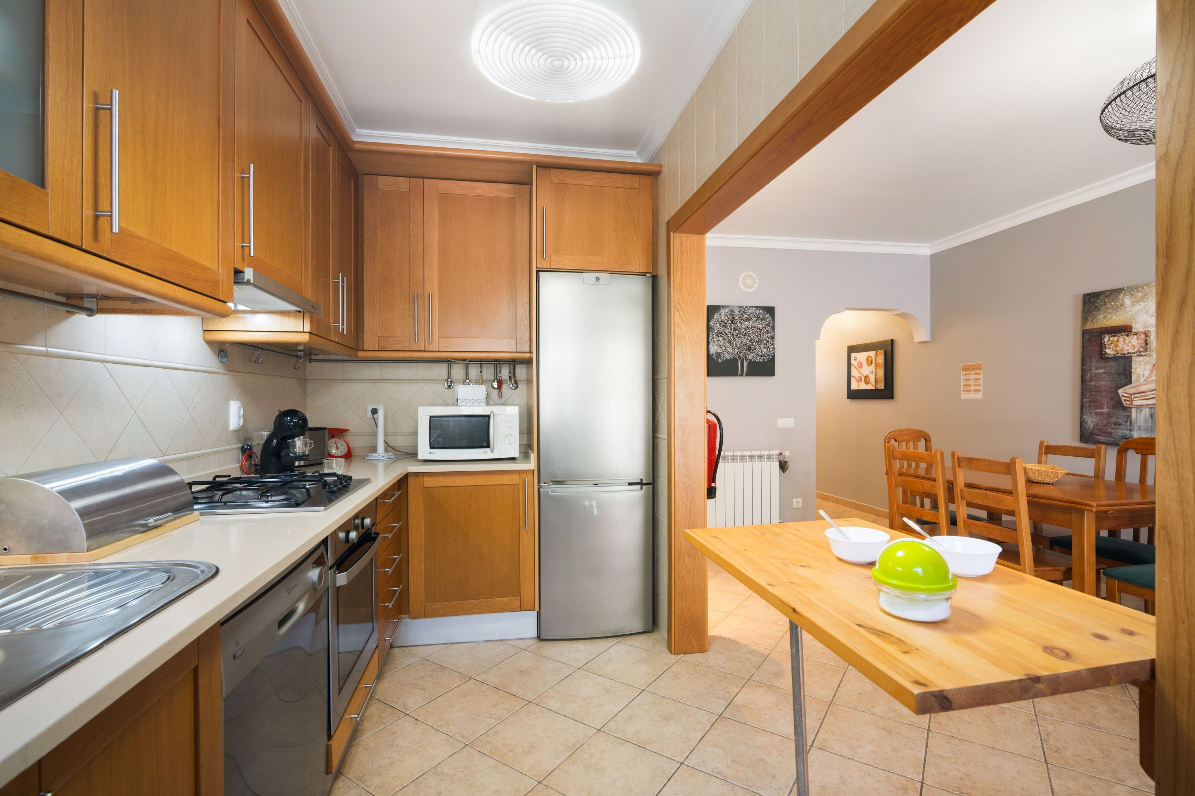 Una cocina compacta con gabinetes de madera, un refrigerador de acero inoxidable, un microondas y una estufa a gas.