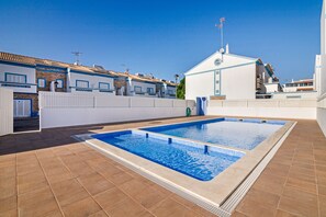 Une piscine dotée d’une terrasse carrelée, entourée d’un mur blanc et d’une clôture.