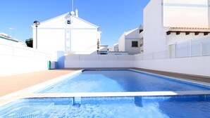 Piscina com borda azulejada, rodeada por edifícios brancos e céu claro.