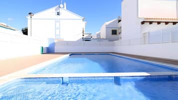 Una piscina con borde de azulejos, rodeada de edificios blancos y un cielo despejado.