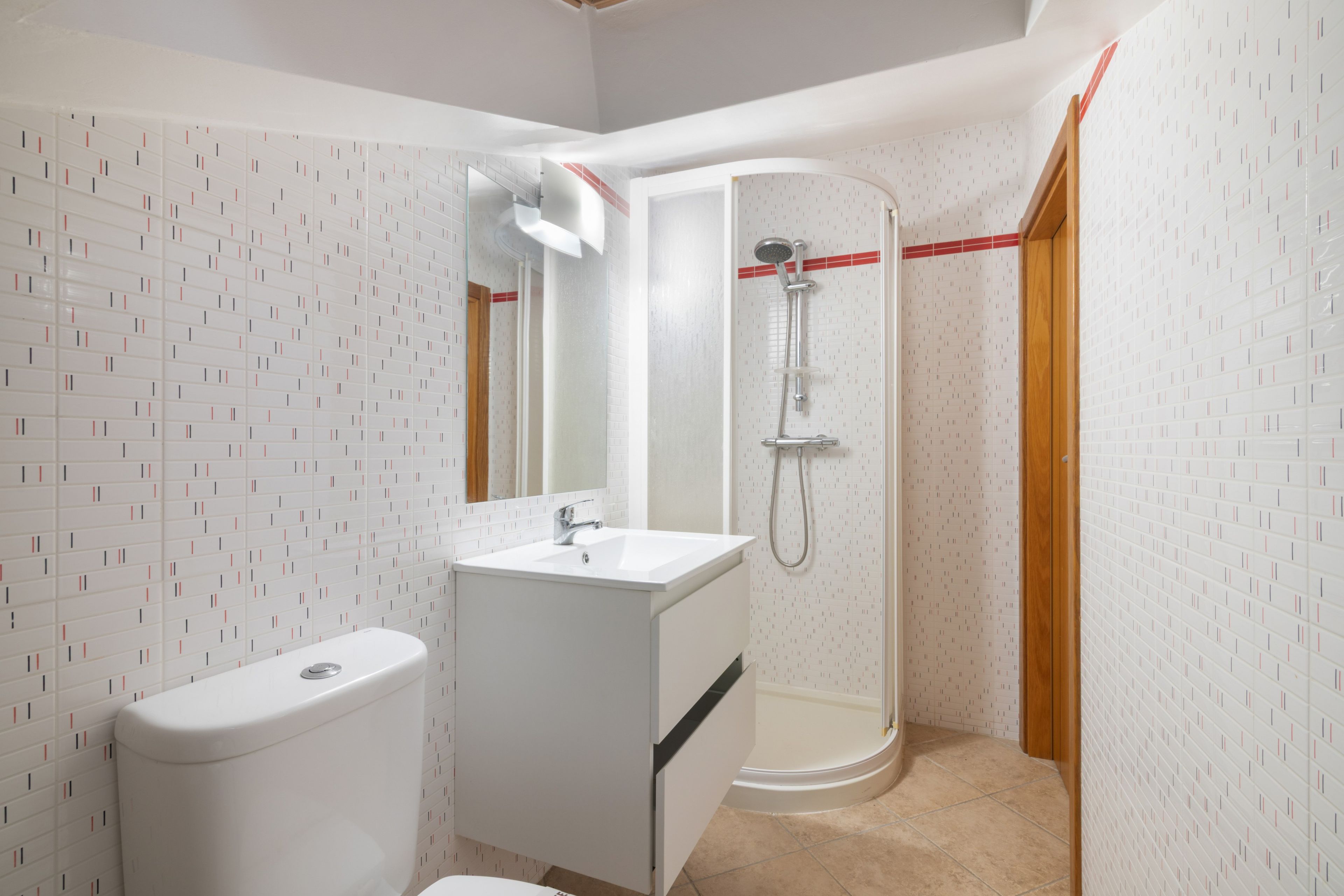 Un baño con inodoro, lavamanos, espejo, ducha y paredes de azulejos.