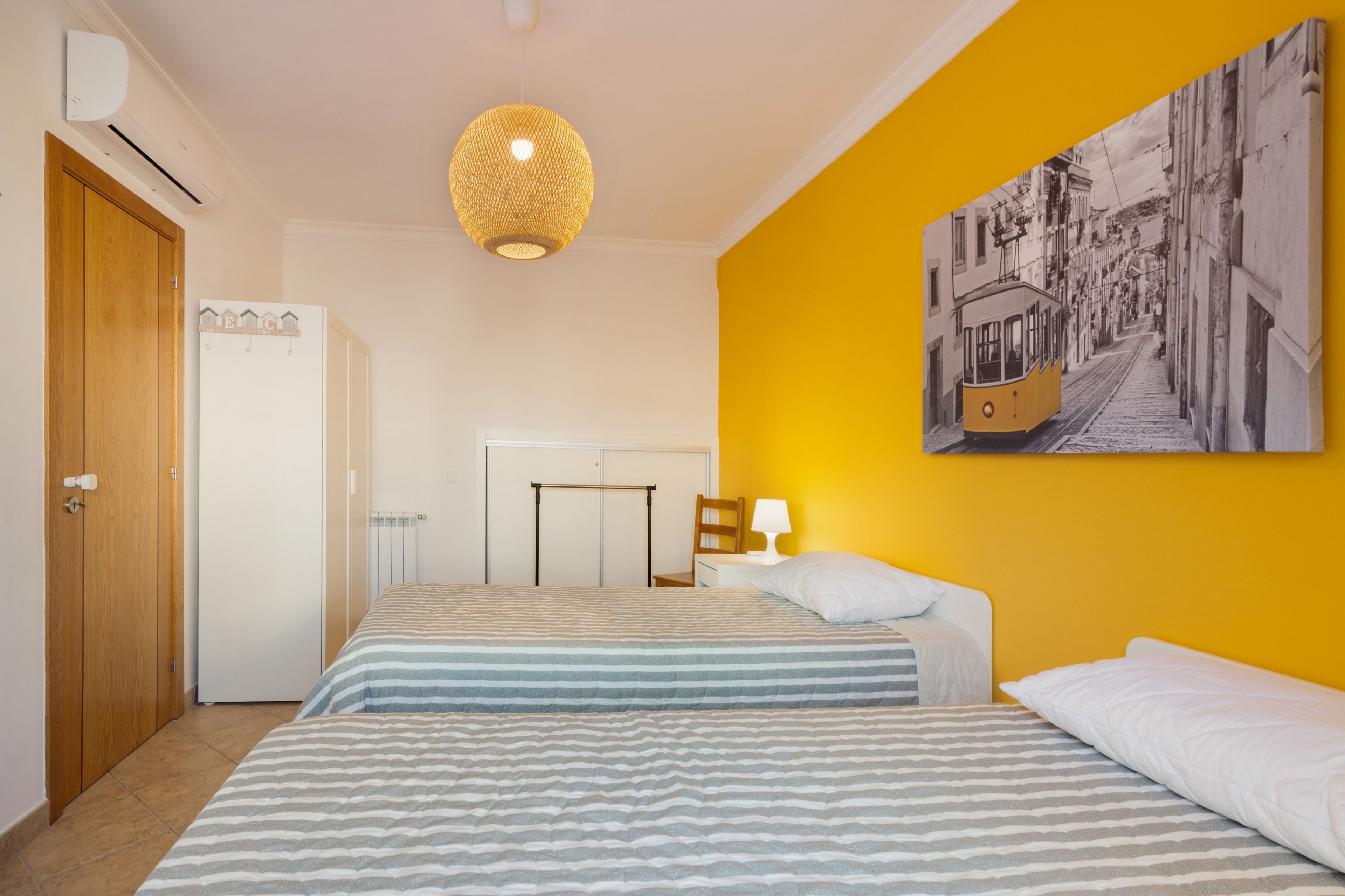 Habitación de hotel con dos camas, una lámpara colgante, un cuadro en la pared y una puerta con perchero.