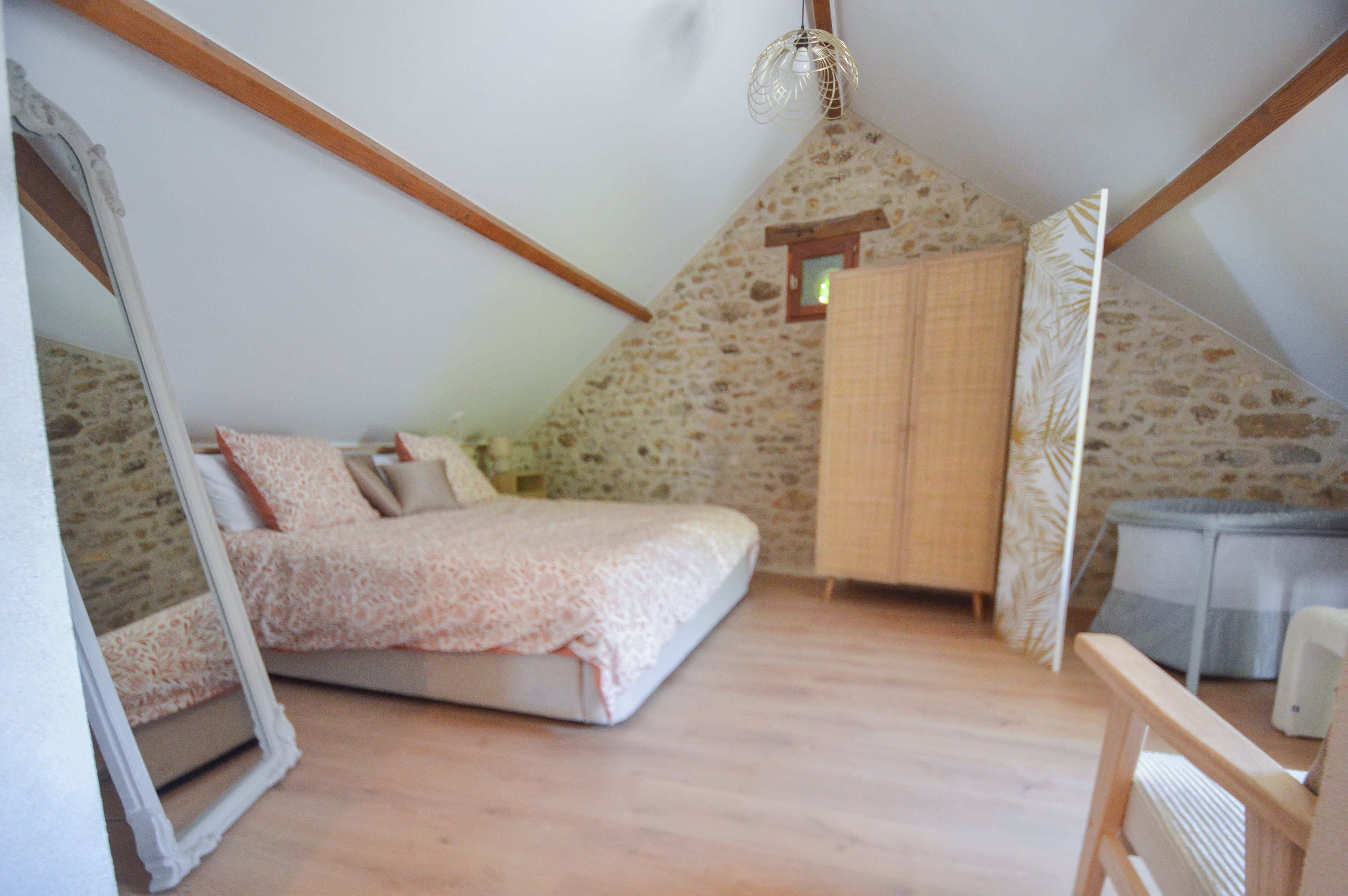 Une chambre avec un plafond en pente, un lit, une armoire et un luminaire suspendu.