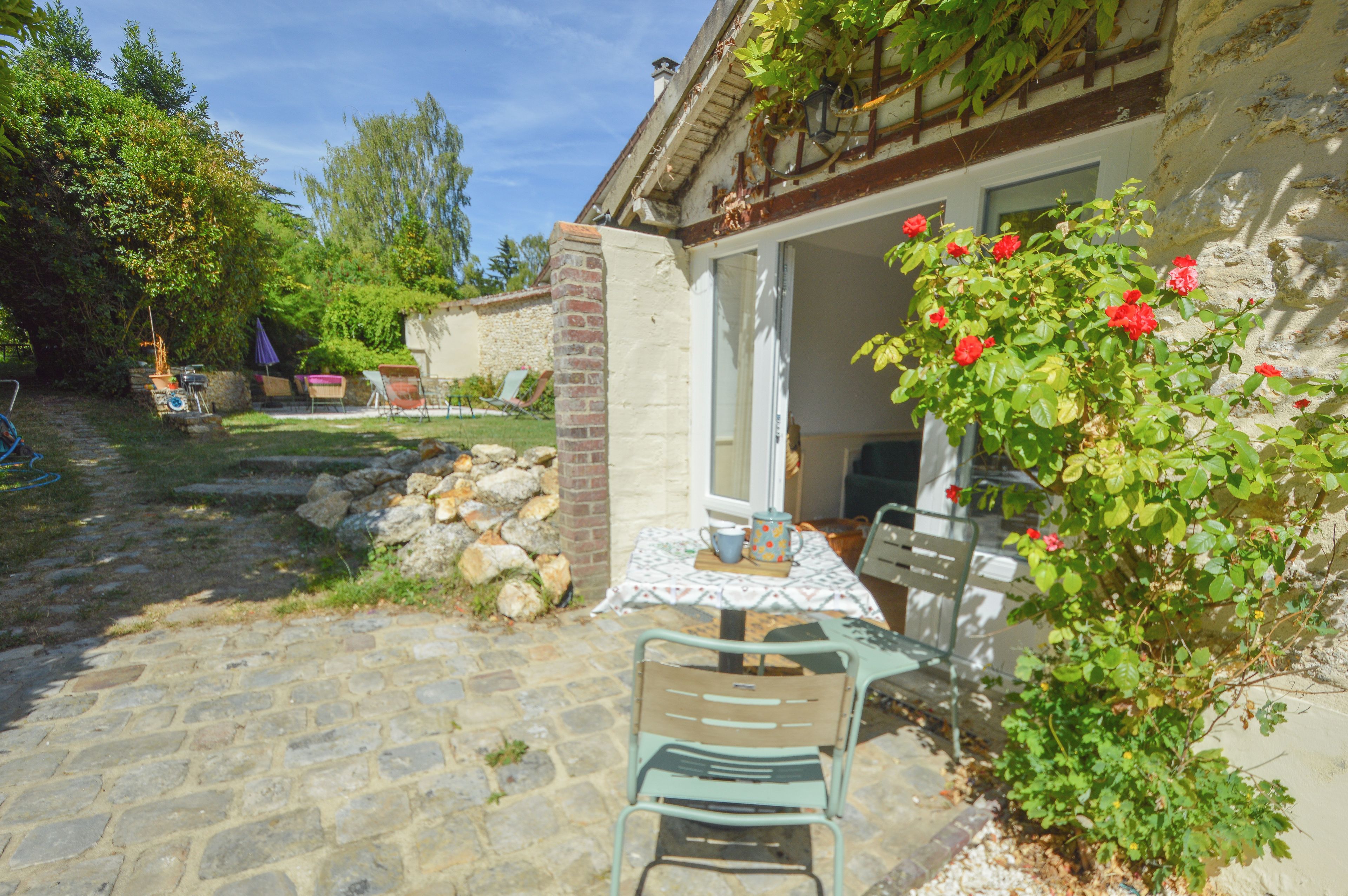 Une terrasse en pierre avec une table et des chaises, un mur en briques et un jardin agrémenté de fleurs rouges.
