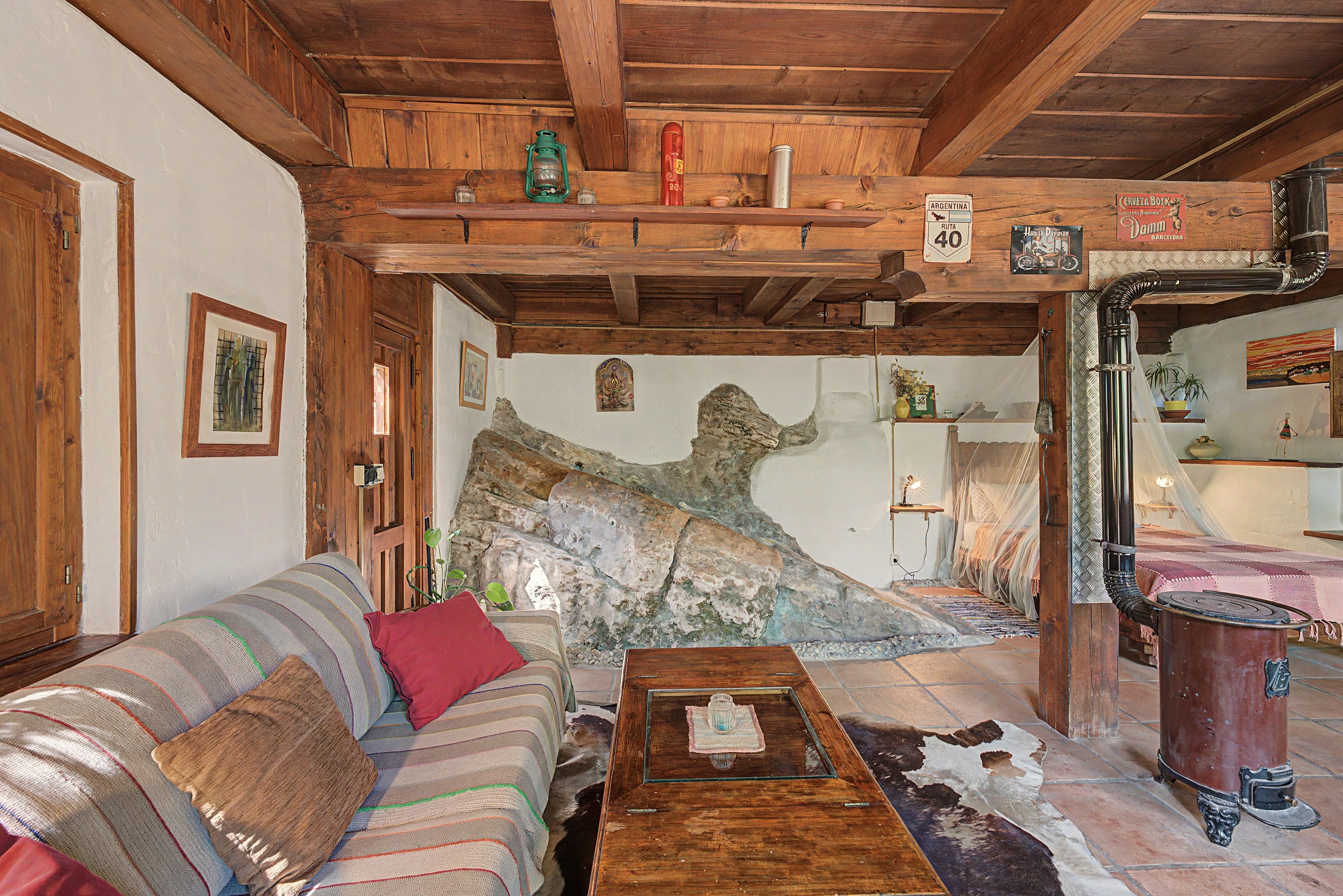 Una habitación rústica con techo de madera, un sofá, una mesa de centro y una pared de piedra con un mural.