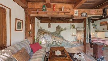 Una habitación rústica con techo de madera, un sofá, una mesa de centro y una pared de piedra con un mural.