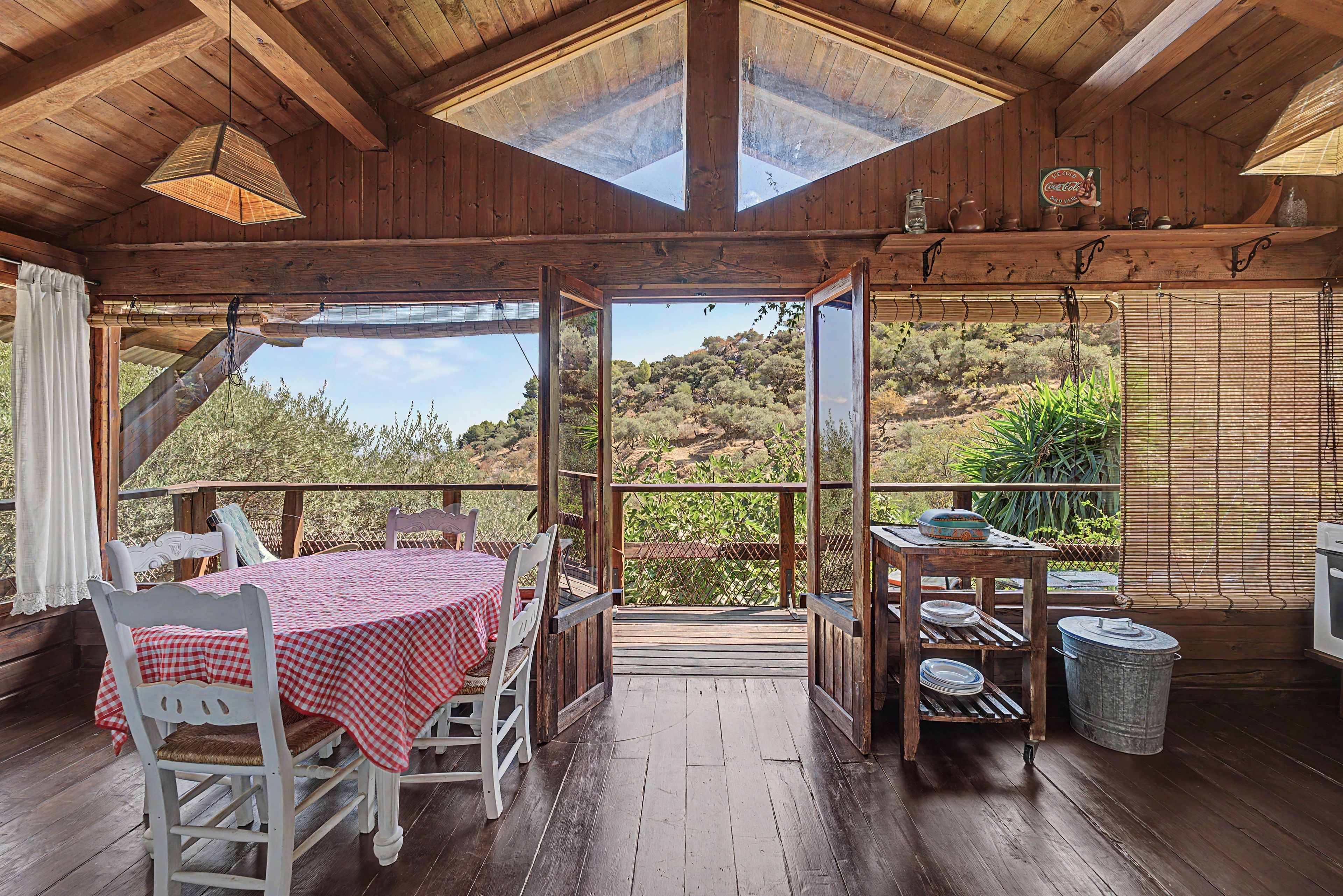 Una cabaña de madera con comedor, una mesa cubierta con mantel a cuadros y vistas del paisaje circundante.