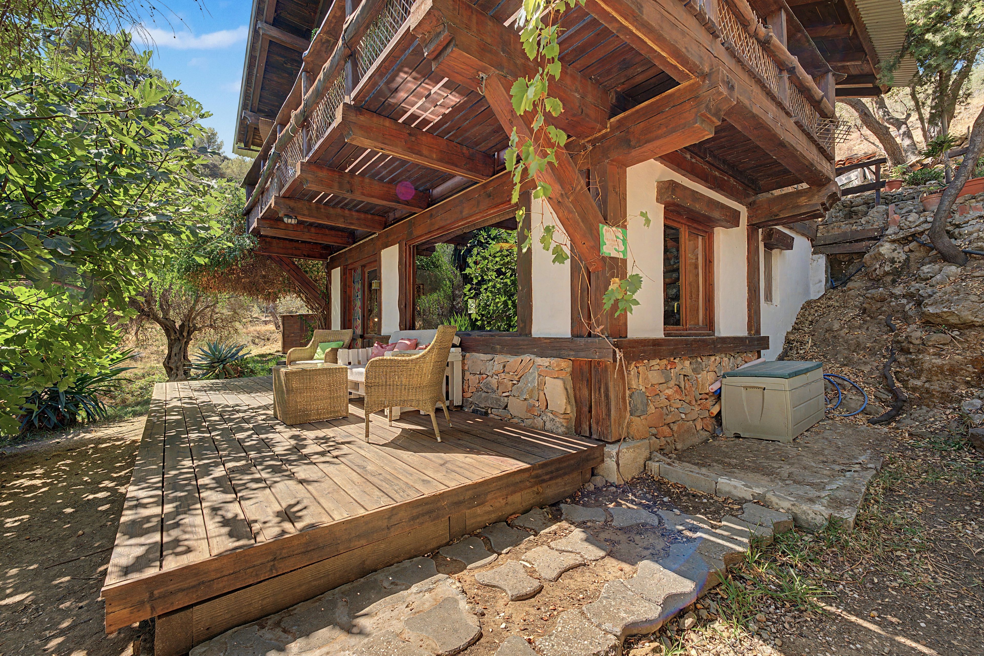 Una casa de madera rústica con base de piedra, una terraza de madera y asientos exteriores.
