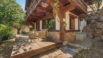 Una casa de madera rústica con base de piedra, una terraza de madera y asientos exteriores.