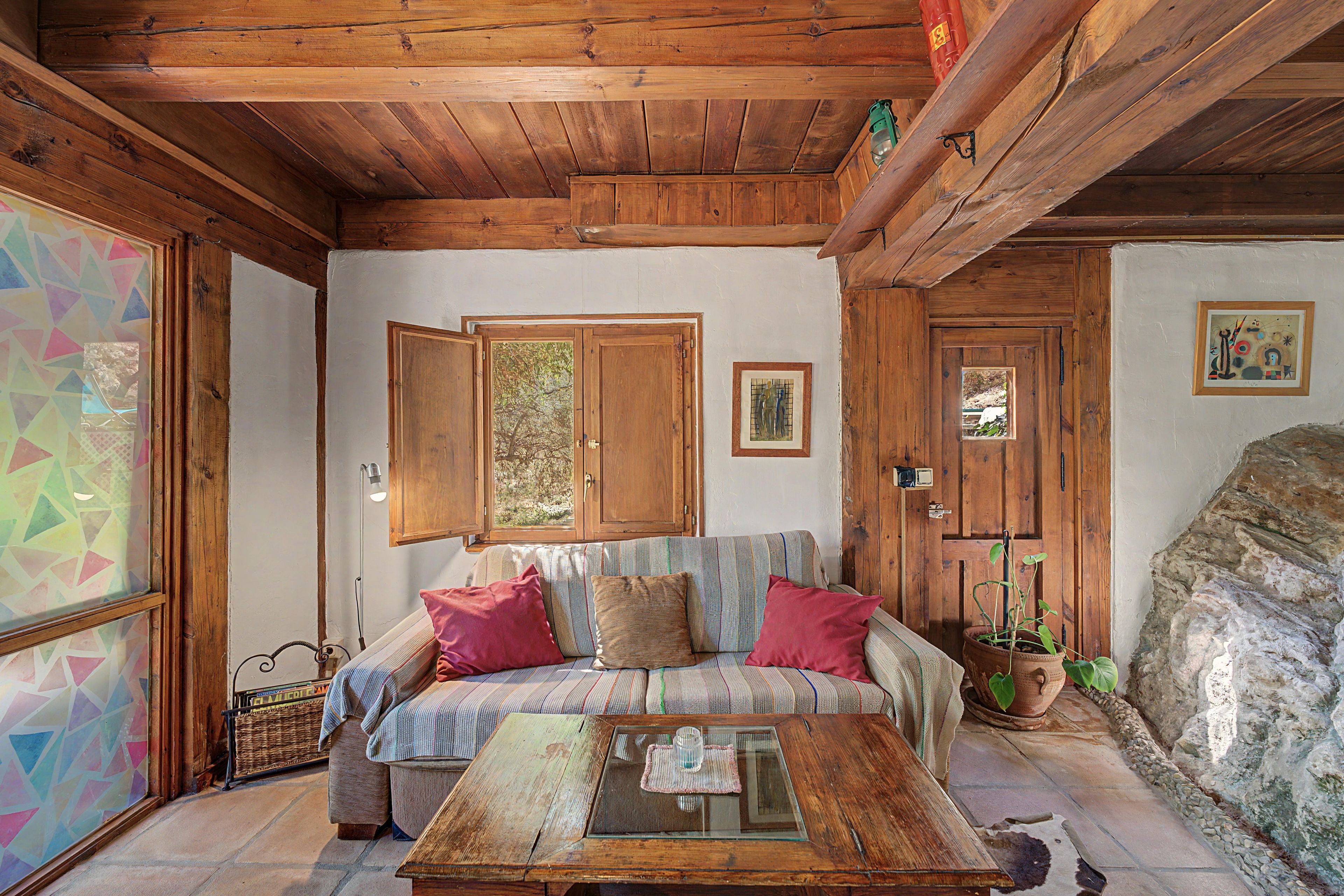 Una habitación acogedora con techo de madera, un sofá con cojines, una mesita de centro y una planta en maceta.