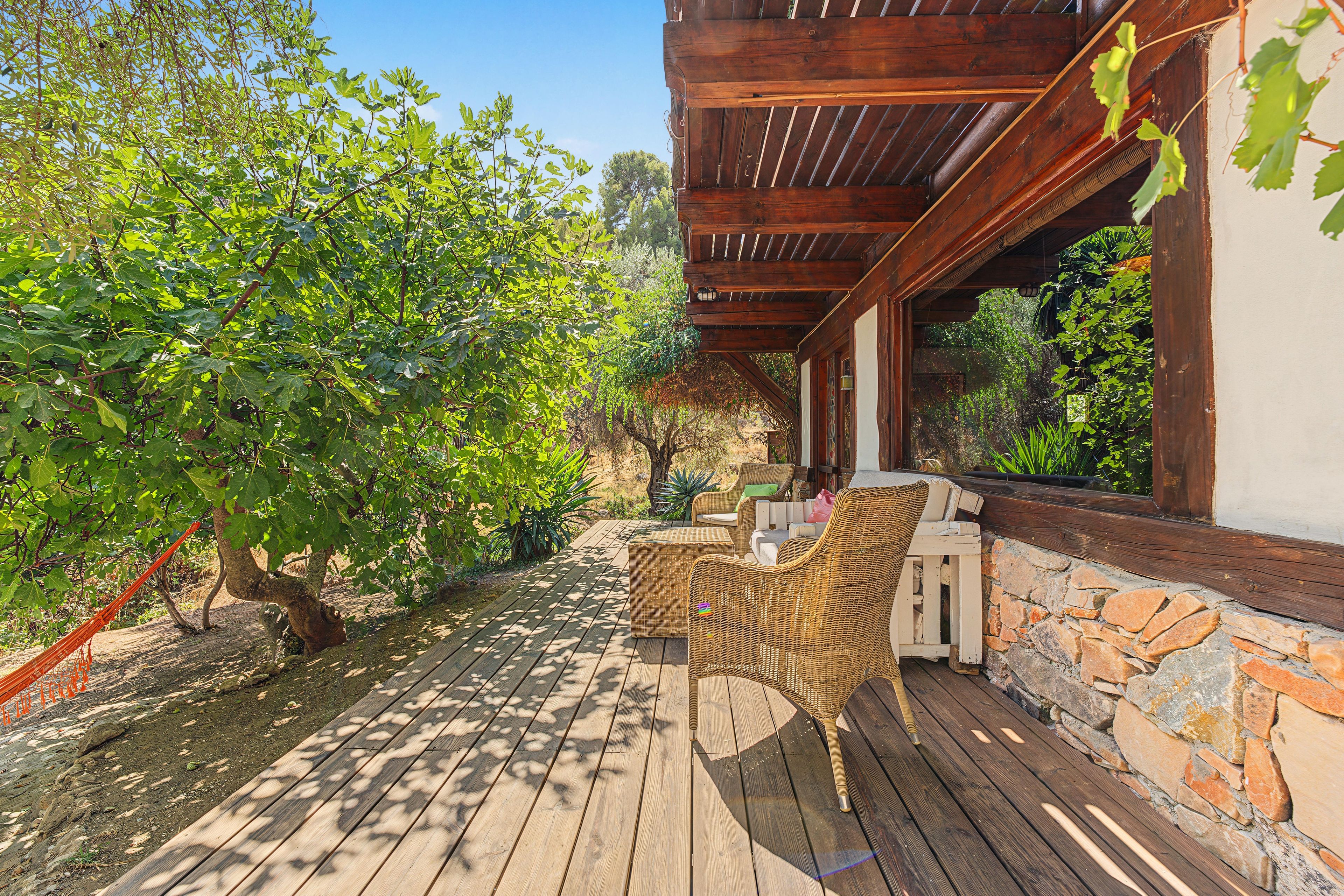 A wooden deck with wicker furniture, a stone wall, and a pergola with vines.