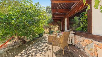 A wooden deck with wicker furniture, a stone wall, and a pergola with vines.