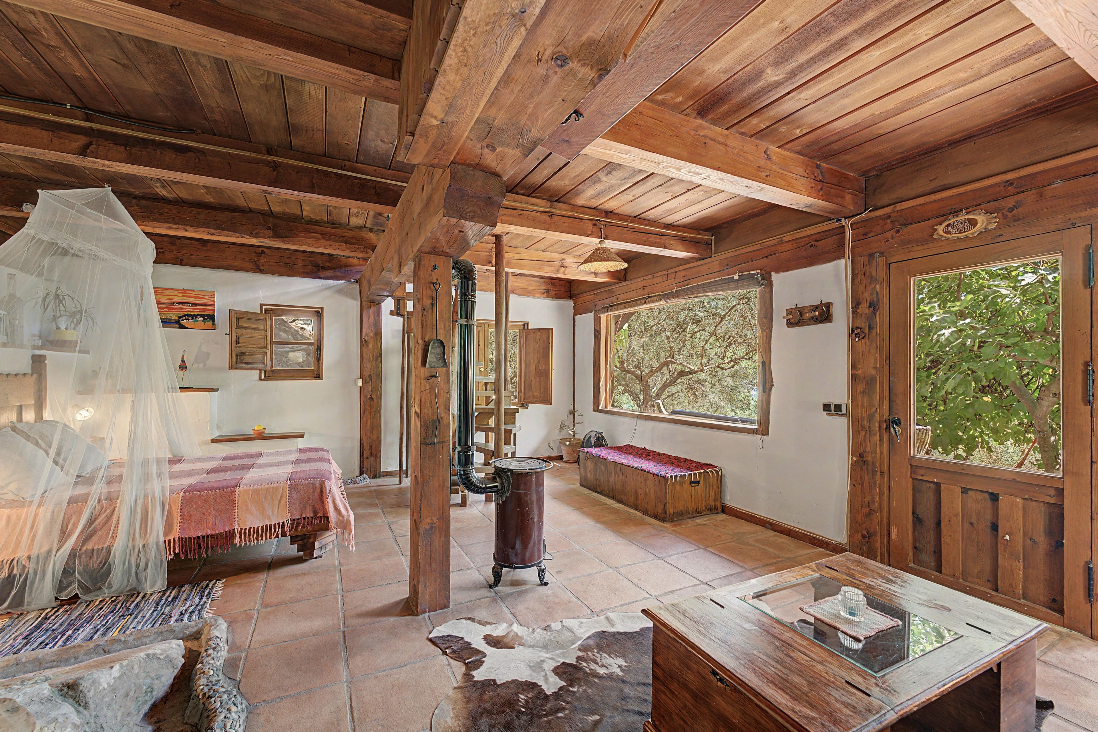 Una habitación rústica de madera con una cama, una mesa con cubierta de vidrio y un ventanal grande.