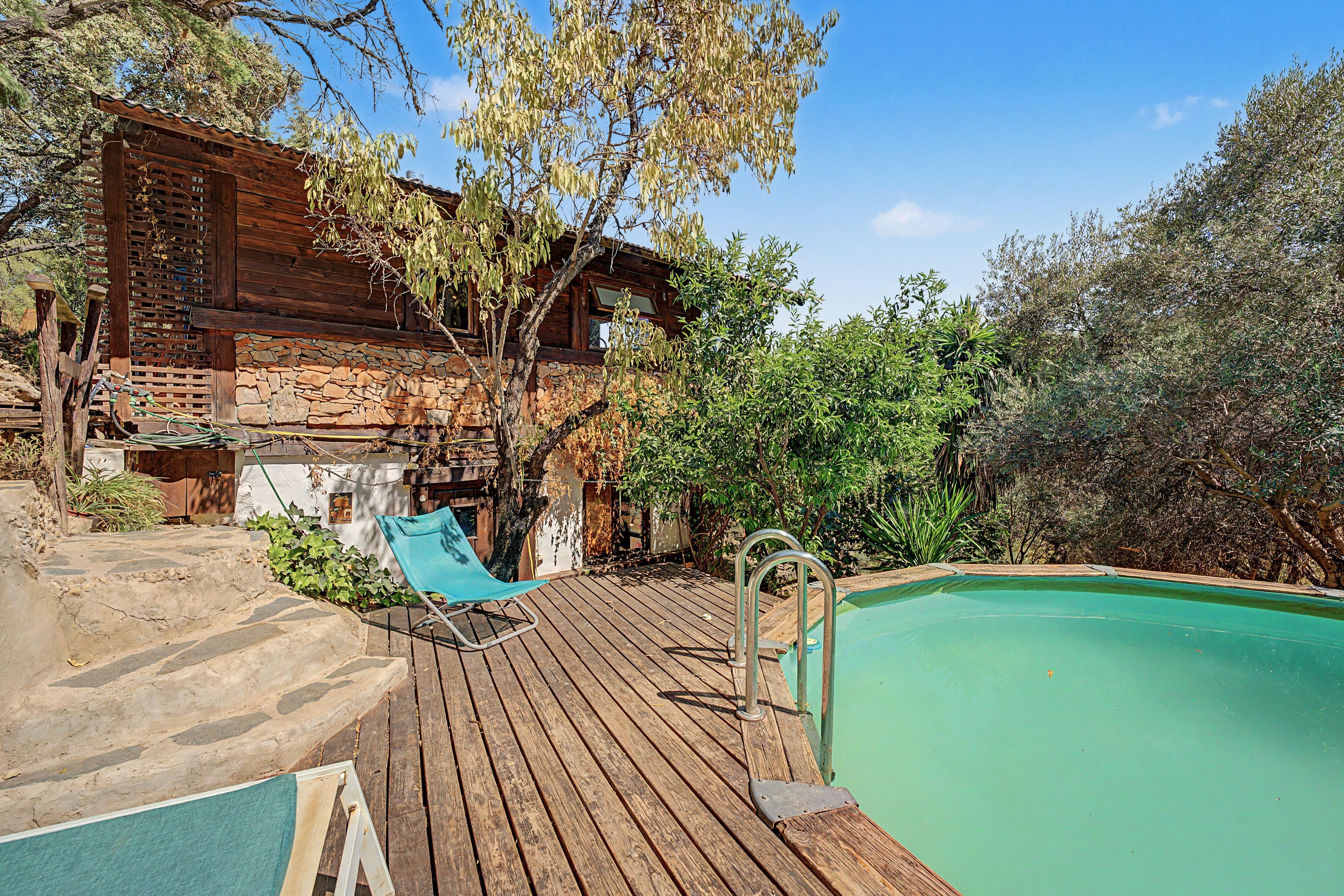 Una terraza de madera con piscina, una silla de descanso y un muro de piedra.