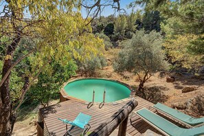 Una terraza de madera con piscina, rodeada de árboles y arbustos.
